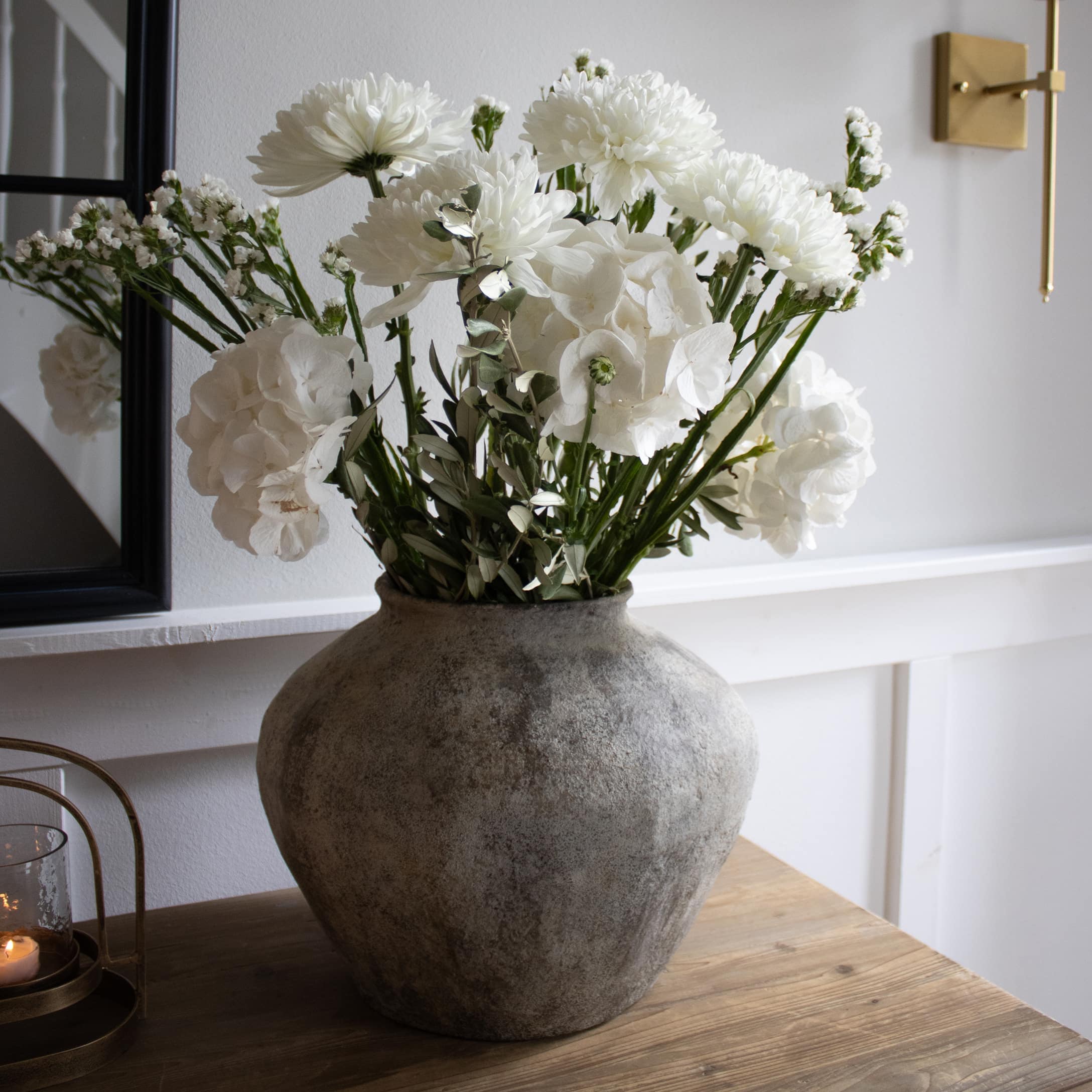 Große graue Steinvase mit weißen Blumen auf Holztisch in modernem Interieur