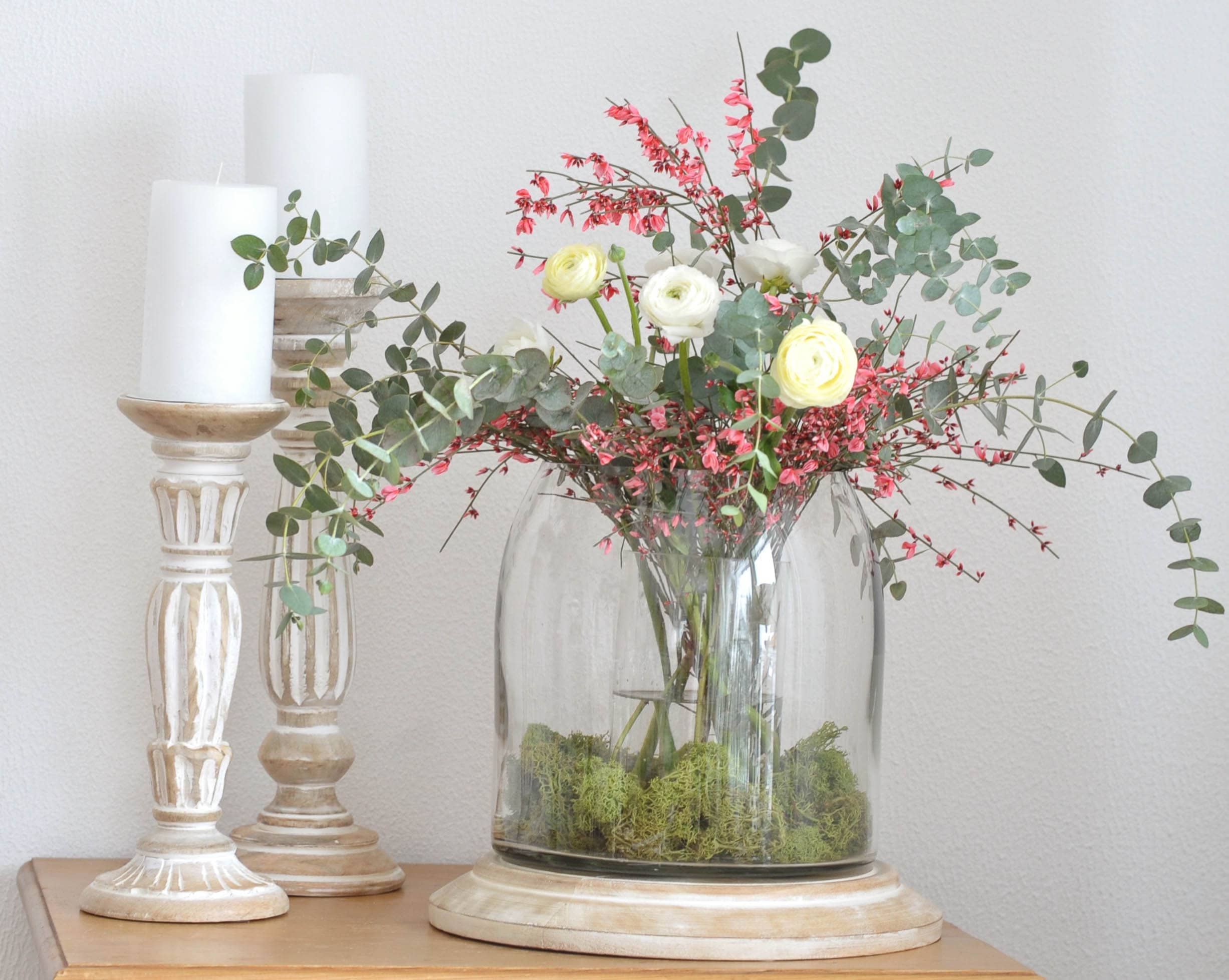 Dekorativer Blumenstrauß mit weißen und rosa Blüten in Glasvase auf Holzsockel mit weißen Kerzen