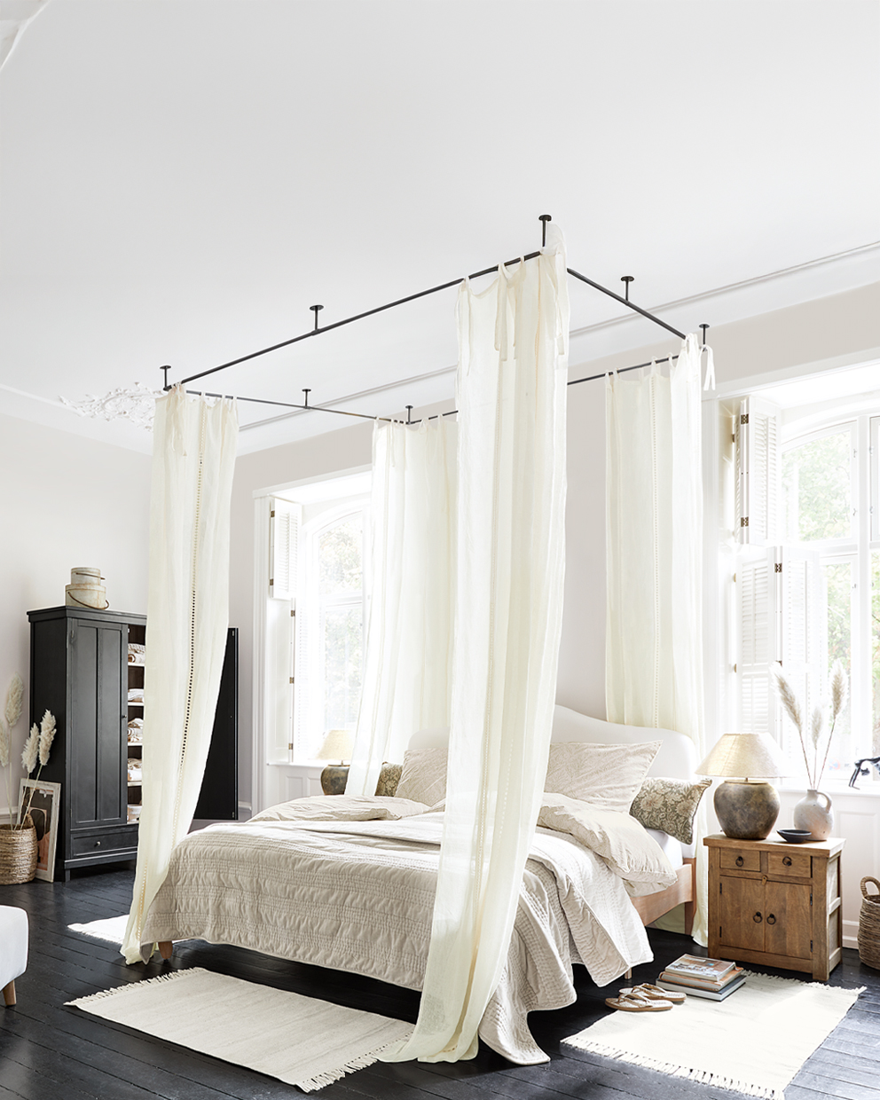 Schlafzimmer mit Himmelbett und cremefarbenen Vorhängen, Holznachttisch und hellen Accessoires