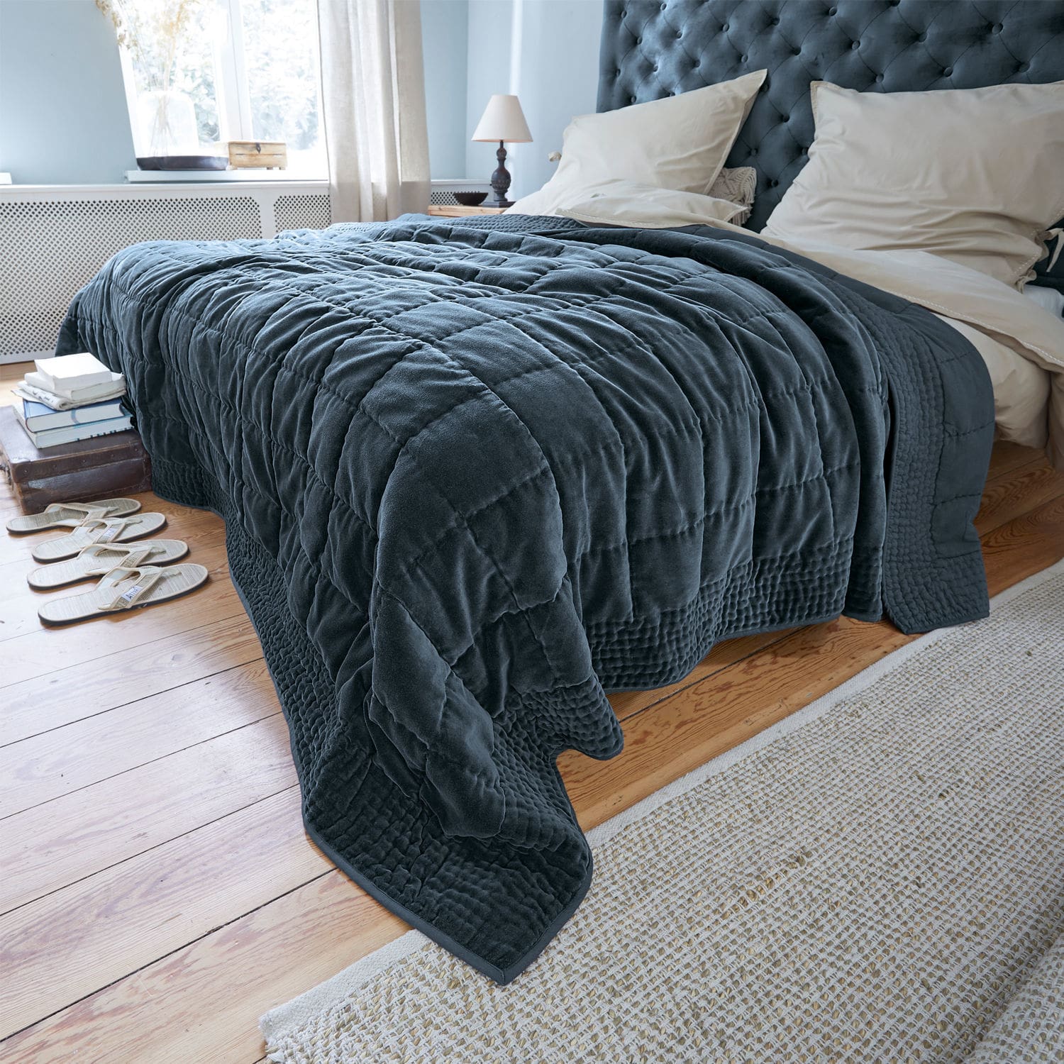 Quilt Arasta Dunkelblauer, gesteppter Kuscheldecke aus weichem Material auf Bett in hellem Schlafzimmer mit Holzboden