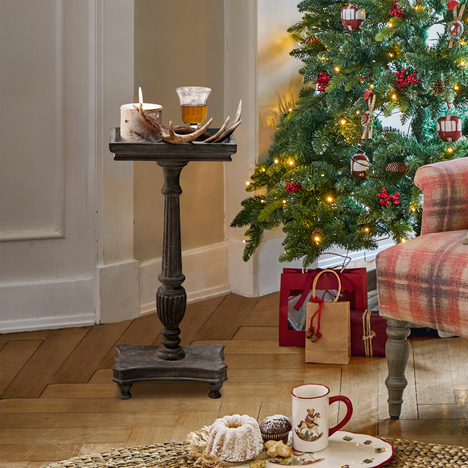 Beistelltisch Caren Dunkler Holzständer mit Kerze und Geweihdeko neben geschmücktem Weihnachtsbaum und Geschenken