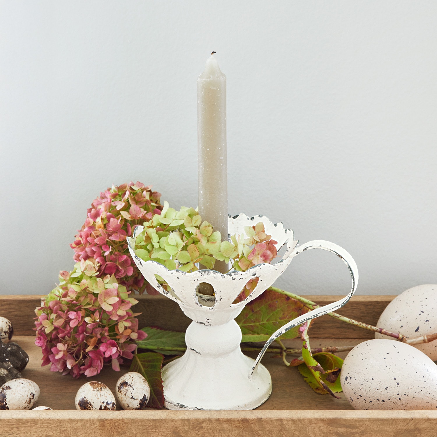 Weißer Metall-Kerzenhalter mit Griff und grauer Kerze, dekoriert mit Blumen und Deko-Eiern