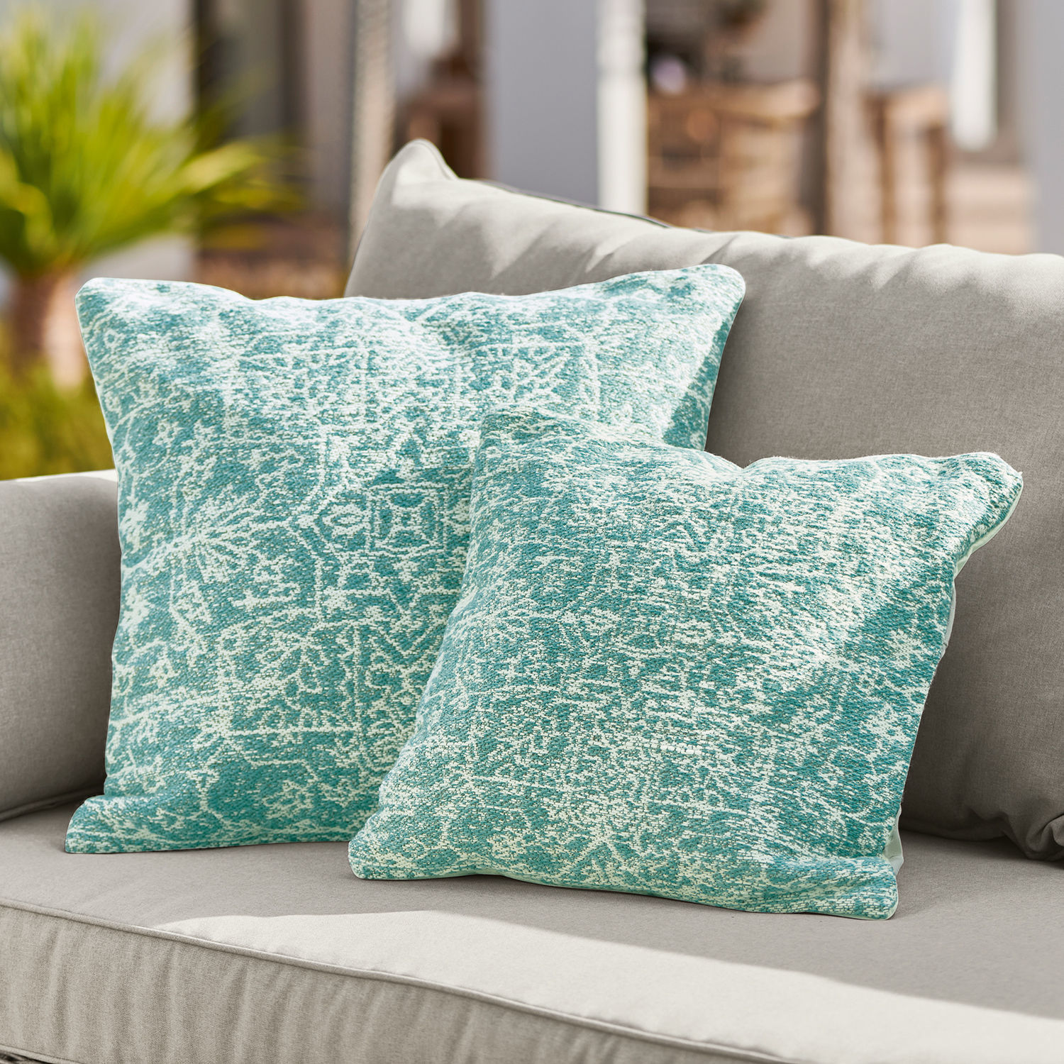 In- & Outdoor-Kissenhülle Bhat Zwei türkis gemusterte Dekokissen auf grauem Sofa, Wohntextilien für Wohnzimmer