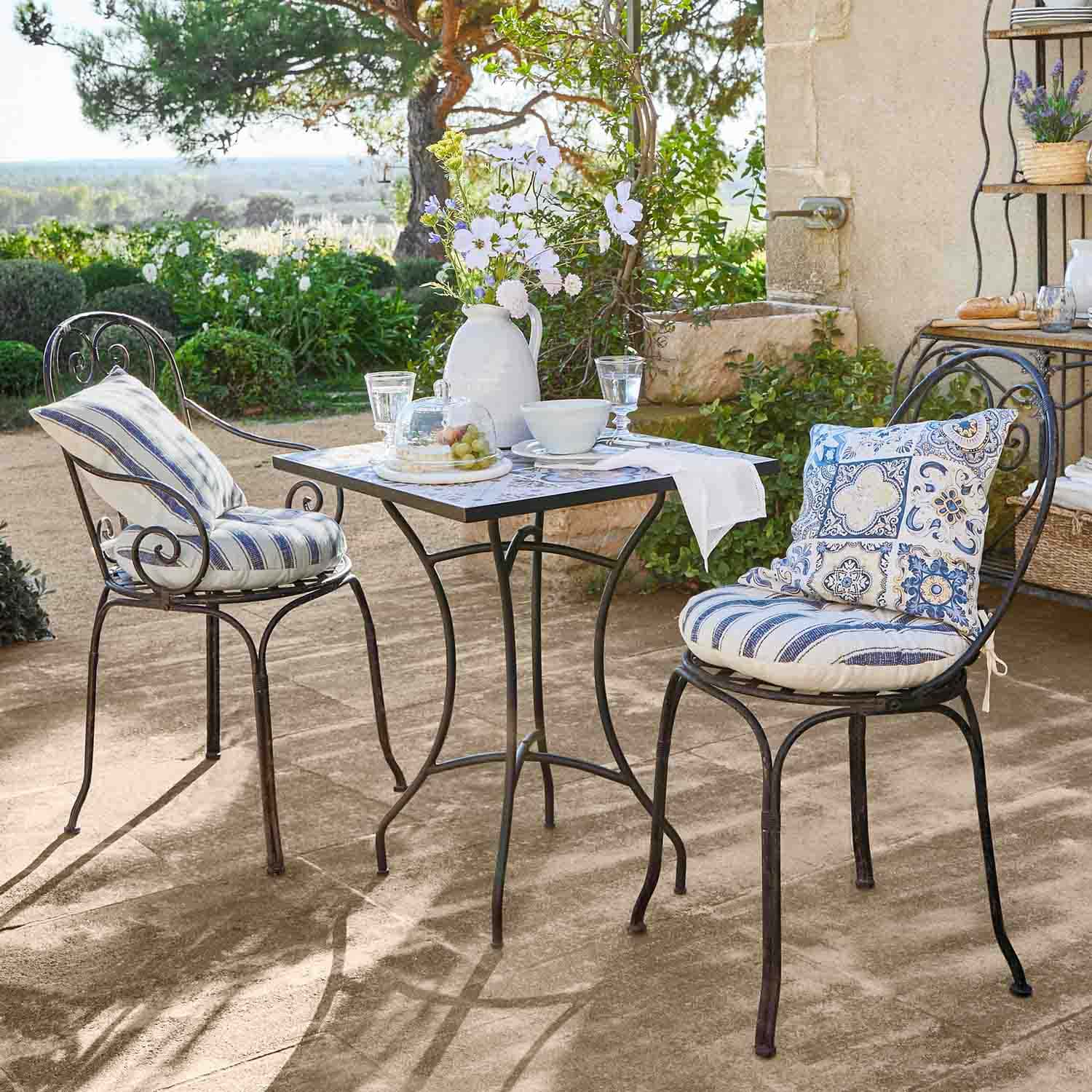 Metalltisch mit quadratischer Platte und zwei Stühle mit blauen Kissen auf sonniger Gartenterrasse
