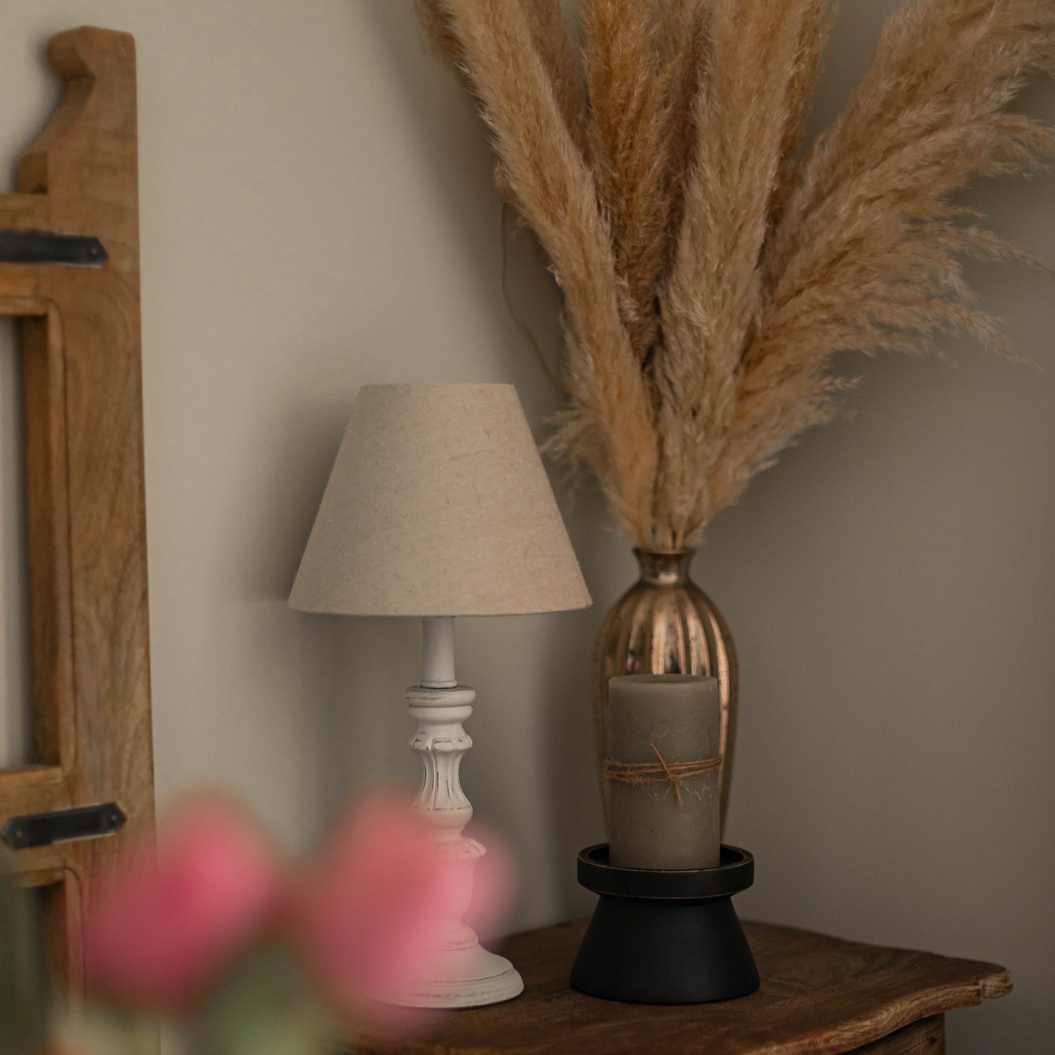 Weiße Holz-Tischlampe mit beigem Lampenschirm und getrockneten Gräsern als Dekoration auf Holztisch