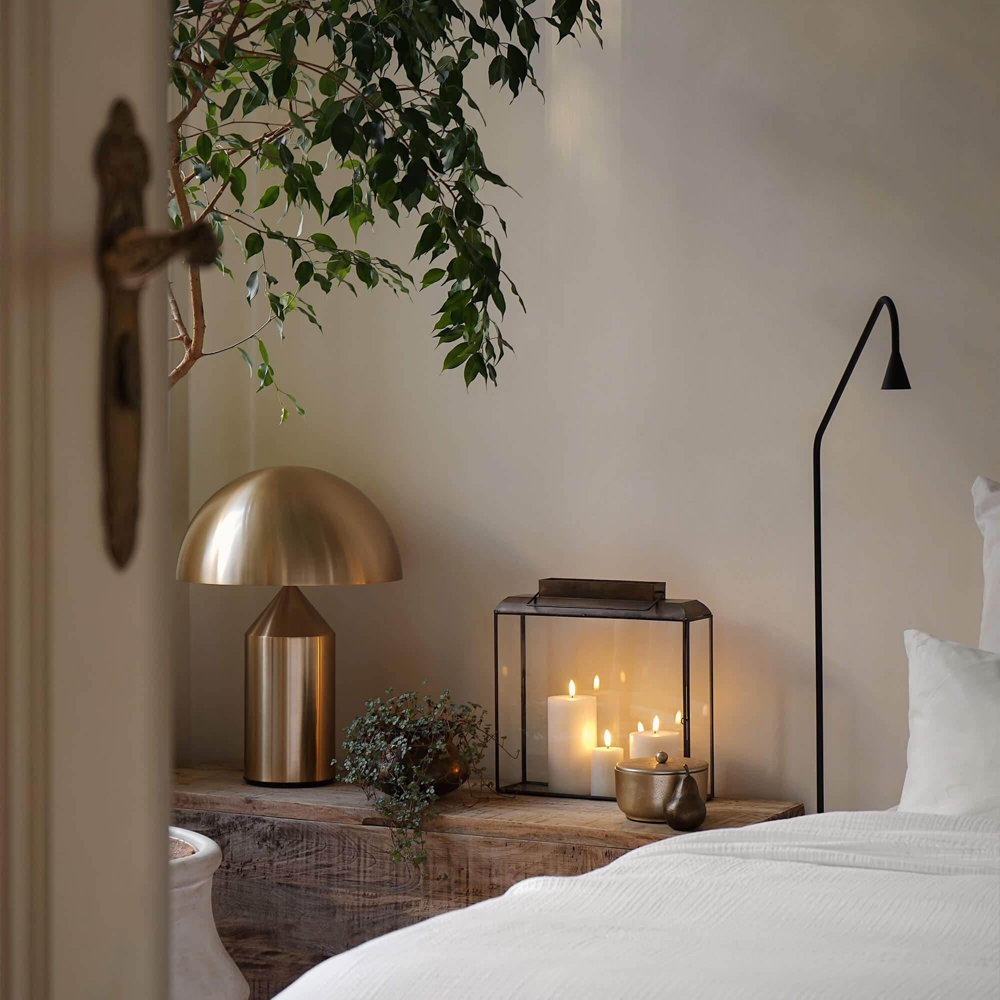 Goldene Metall-Tischlampe und Glaslaterne mit weißen Kerzen auf Holzablage im Schlafzimmer