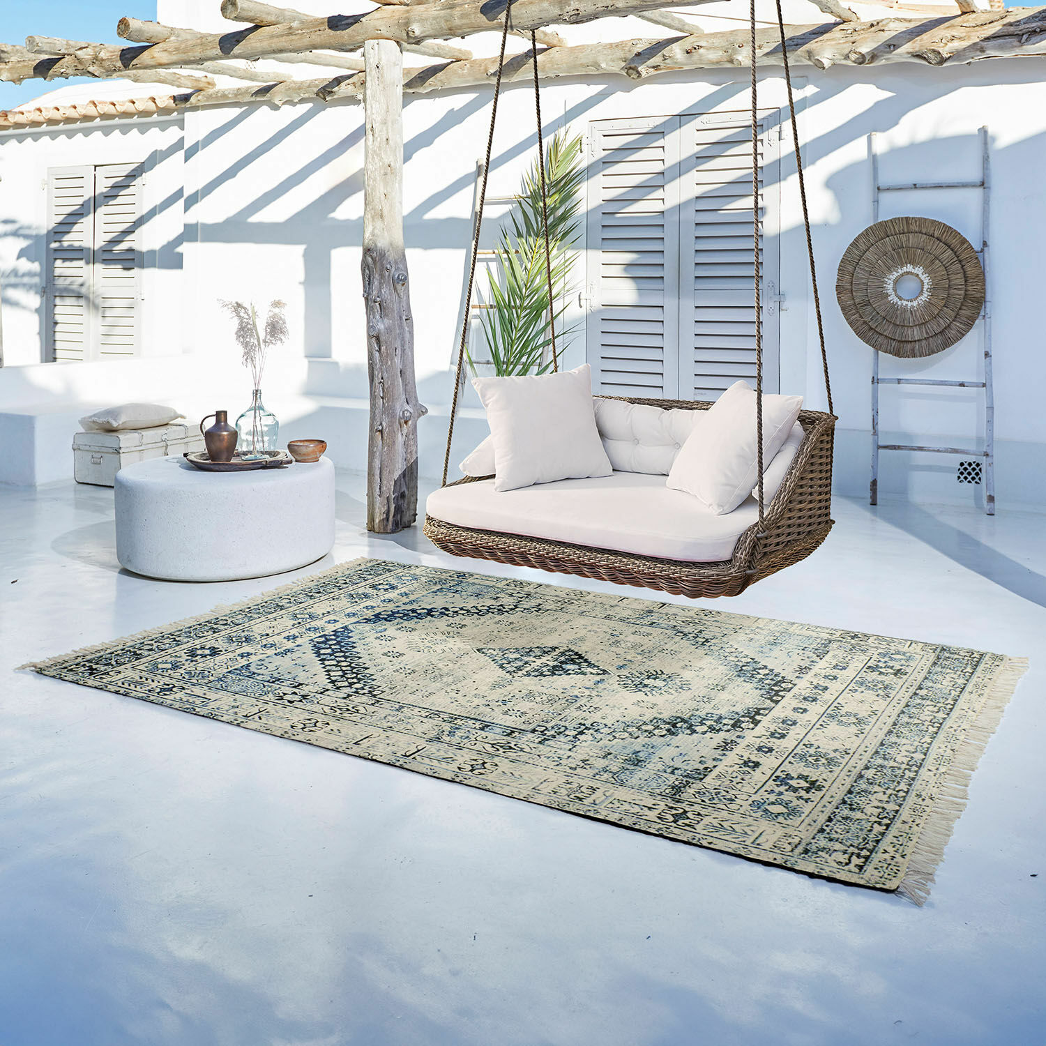 In- & Outdoor-Teppich Daly Vintage Teppich in Beige und Blau auf hellem Boden neben Rattan-Hängesofa mit weißen Kissen