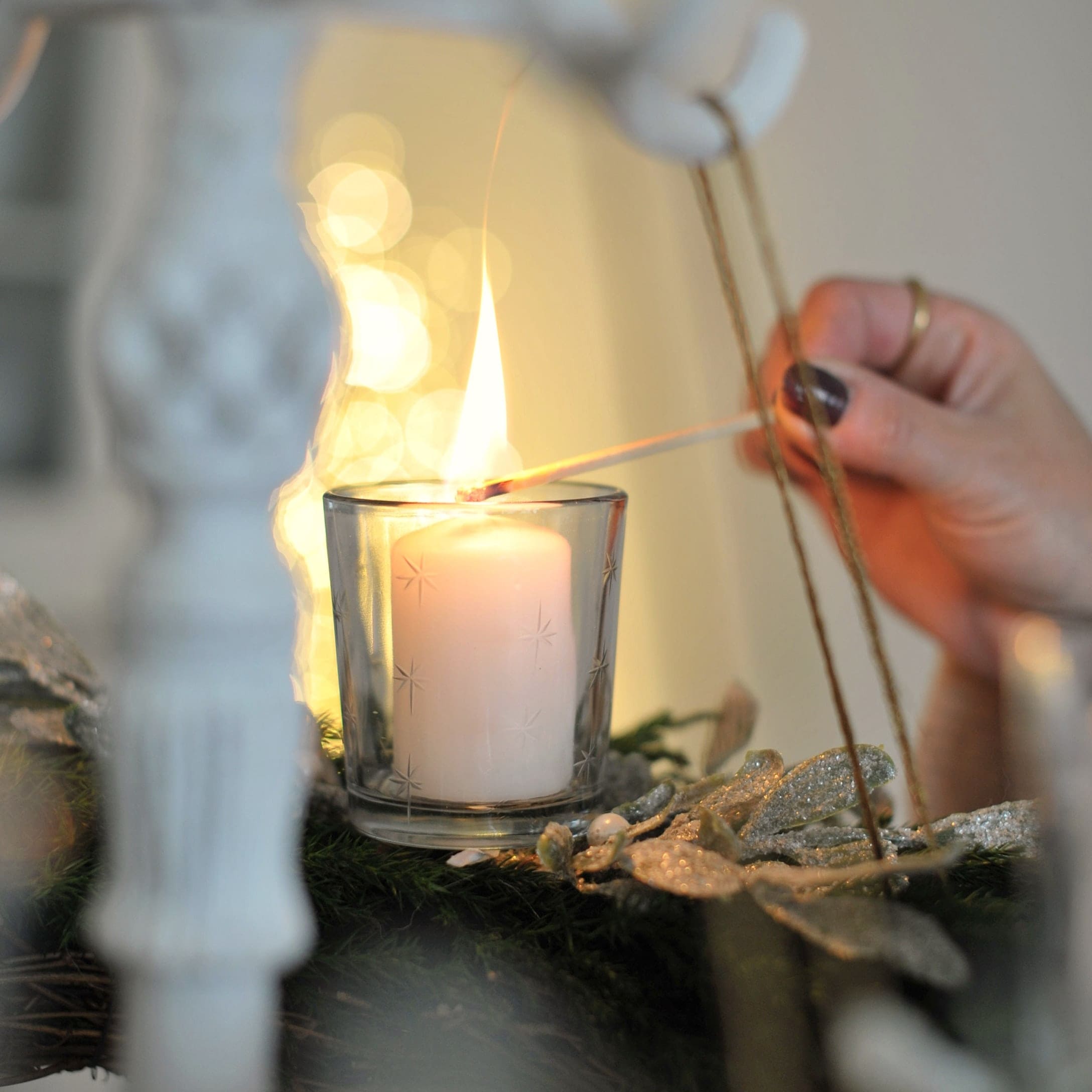 Weiße Kerze im Glaswindlicht auf grünem Adventskranz mit glitzernder Dekoration