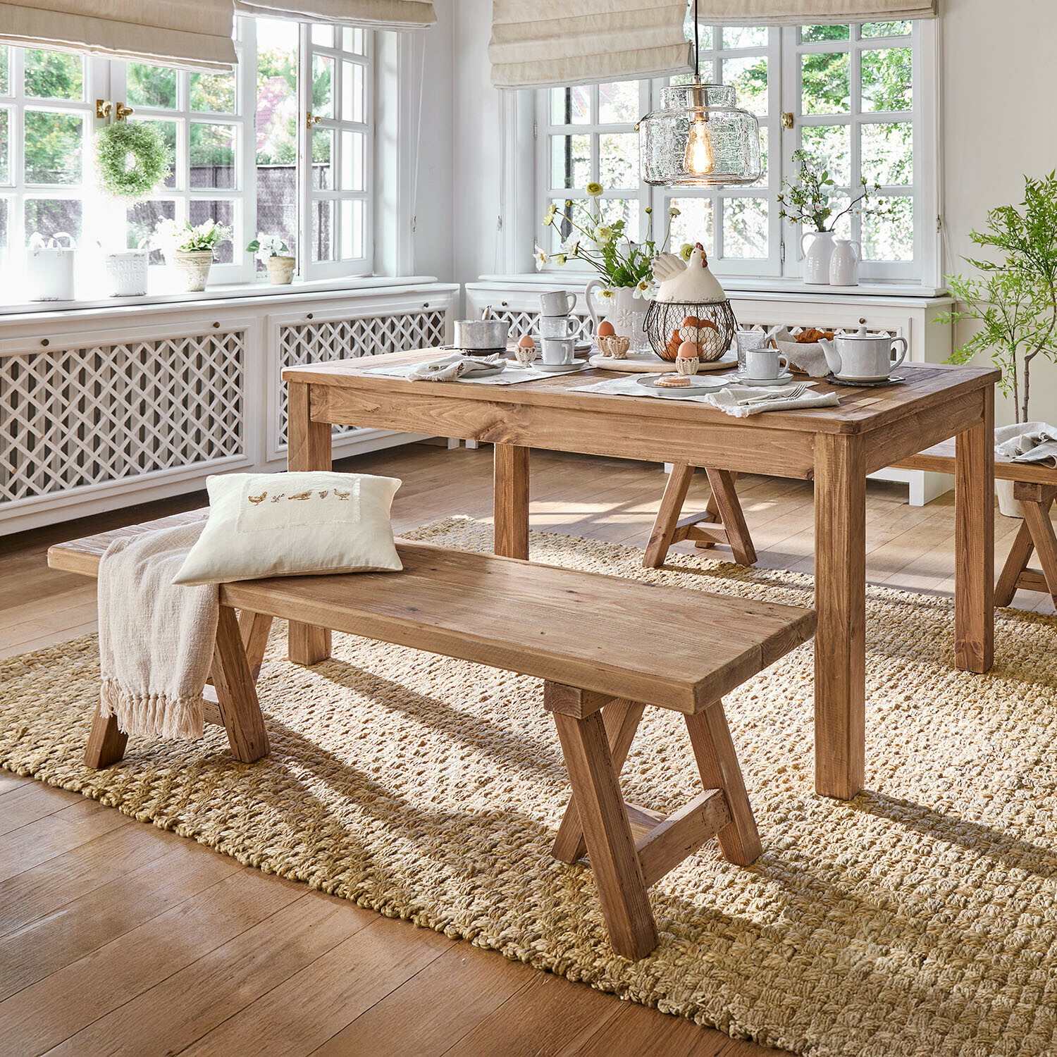 Esszimmer mit Holztisch und Bank auf natürlichem Teppich, helles Zimmer mit großen Fenstern
