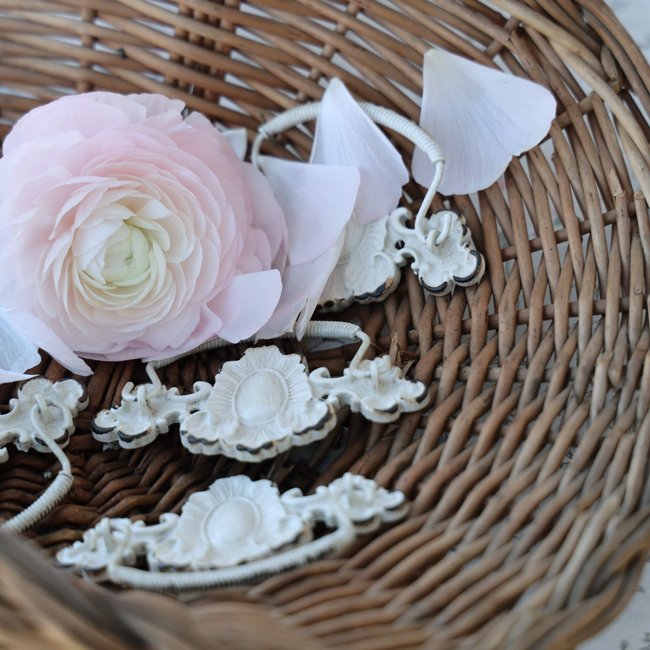 Zarte rosa Blume und weiße Metallgriffe in einem Korb aus Weide, Vintage-Innendekoration