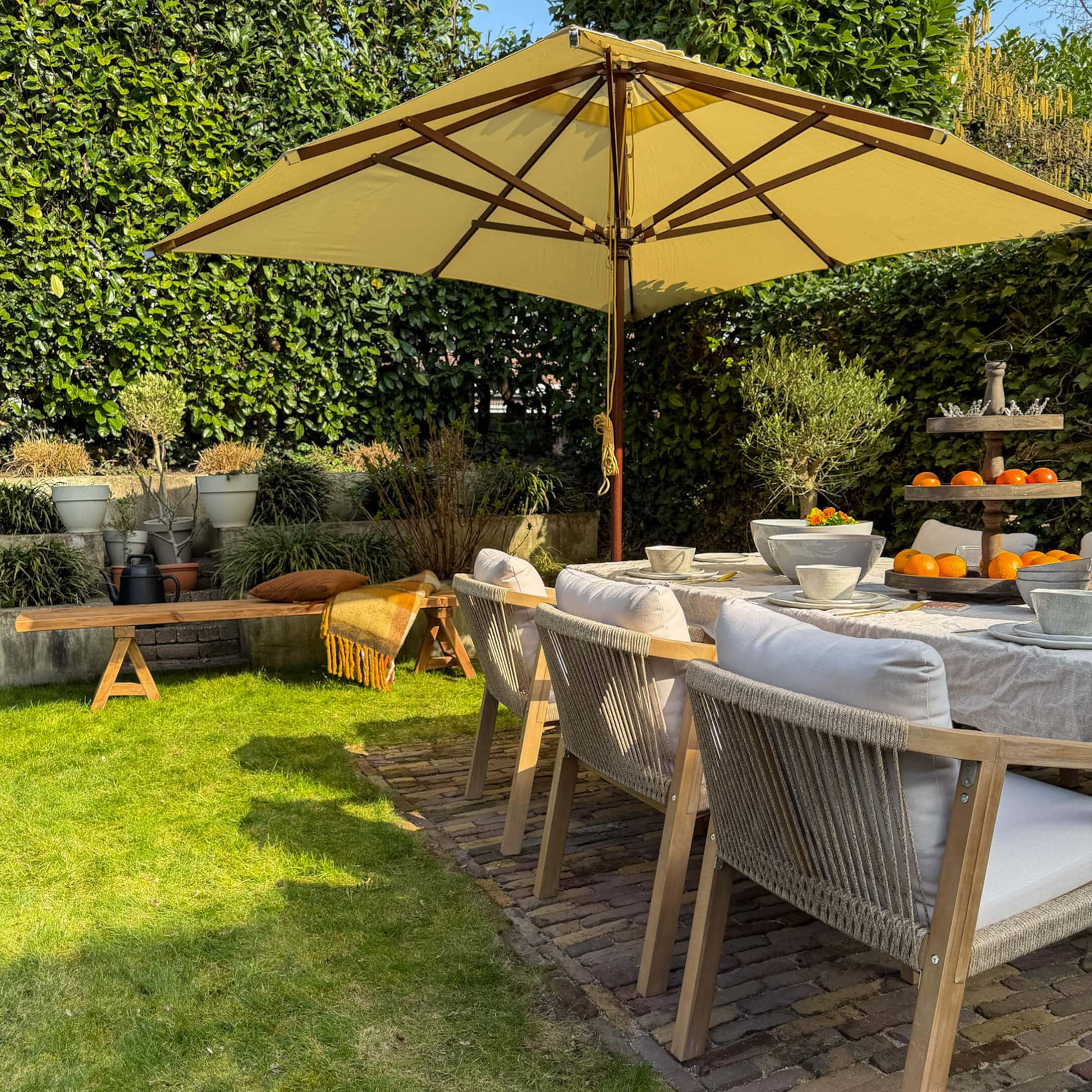 Gartenmöbel-Set mit Holzstühlen und gelbem Sonnenschirm auf grünem Rasen im sonnigen Garten