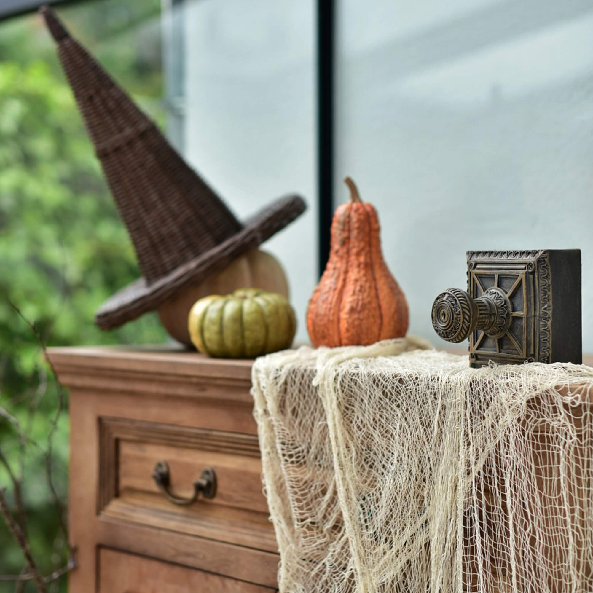 Holzkommode mit Hexenhut aus Korbgeflecht und Kürbissen als Halloween-Dekoration