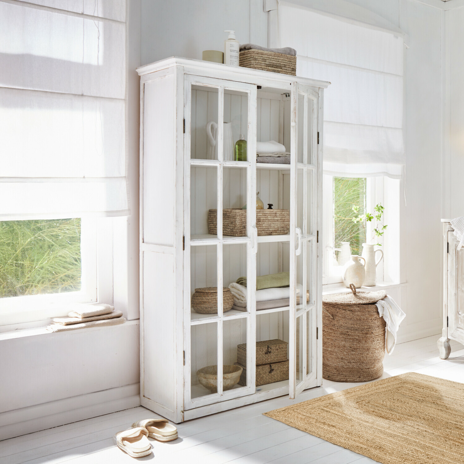 Weiße Holzvitrine mit Glastüren in hellem Raum mit natürlichen Dekorationen und Textilien