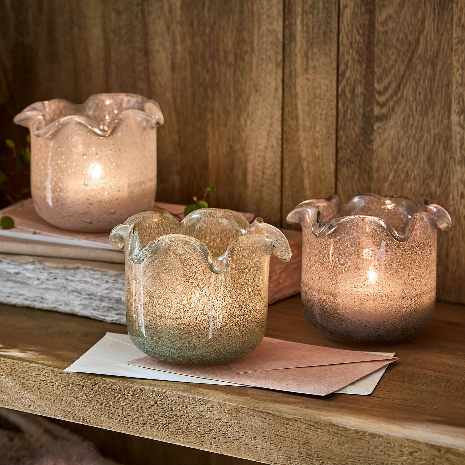 Drei dekorative Windlichter aus geblasenem Glas in Pastellfarben auf einem Holzregal