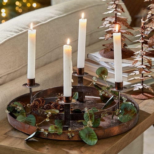 Metall-Adventskranz mit vier weißen Kerzen und Blattdeko auf Holztisch im Wohnzimmer