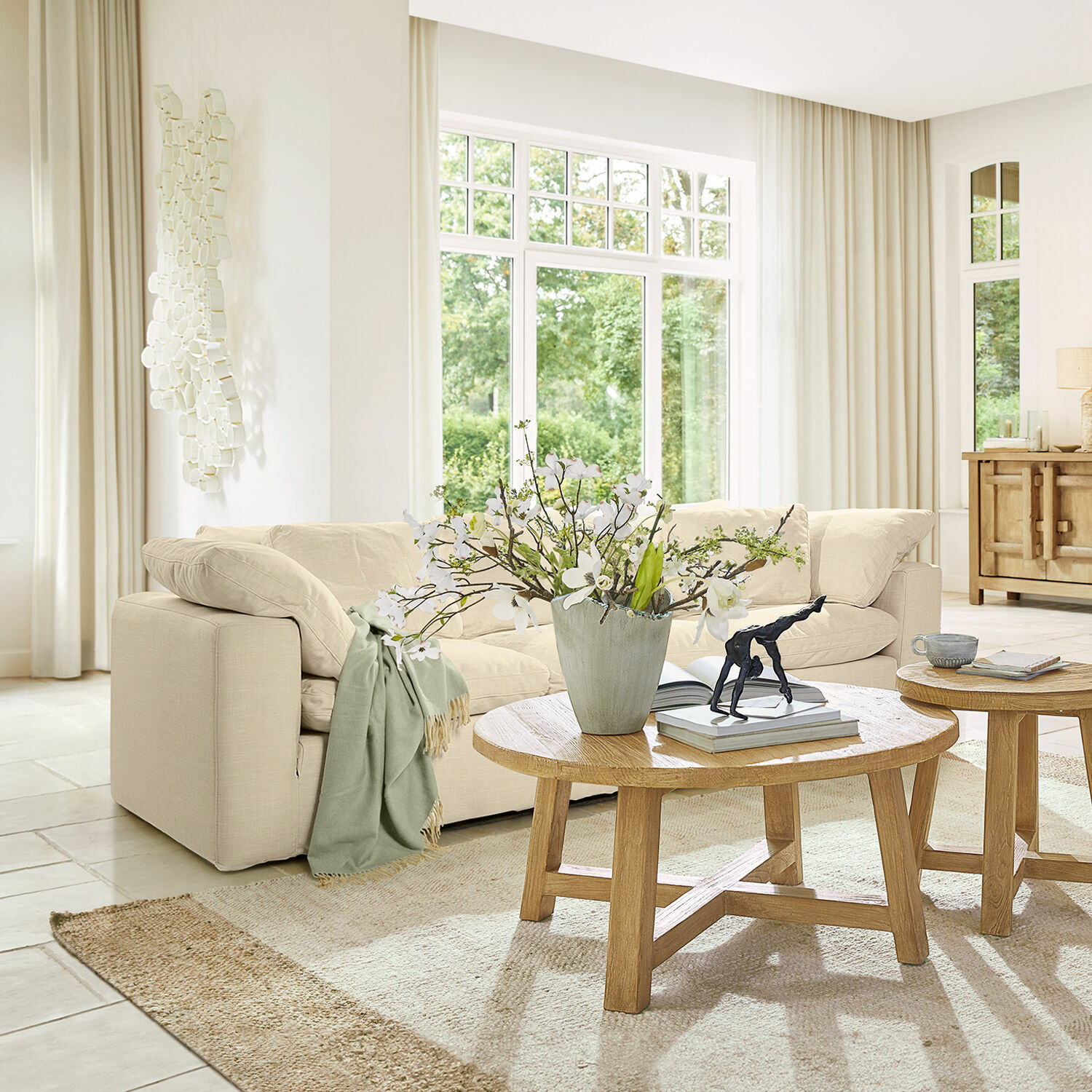 Sofa Queensbridge Hellbeiges Sofa aus Stoff im modernen Wohnzimmer mit Holzcouchtisch und Blumenarrangement