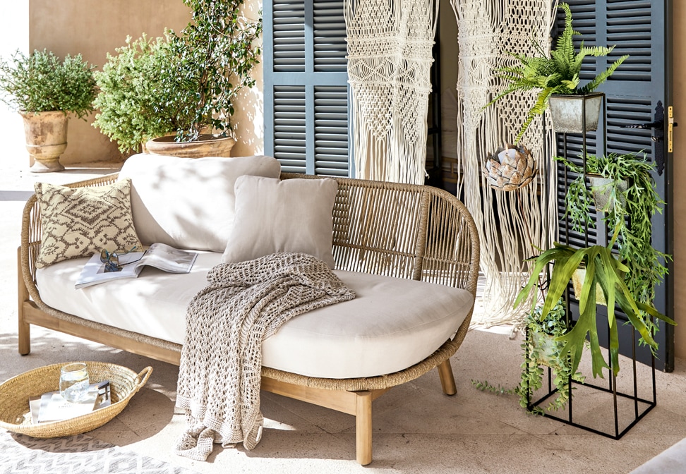 Boho-Sofa mit hellbeigem Polster und Holzrahmen, dekoriert mit Kissen und gestrickter Decke