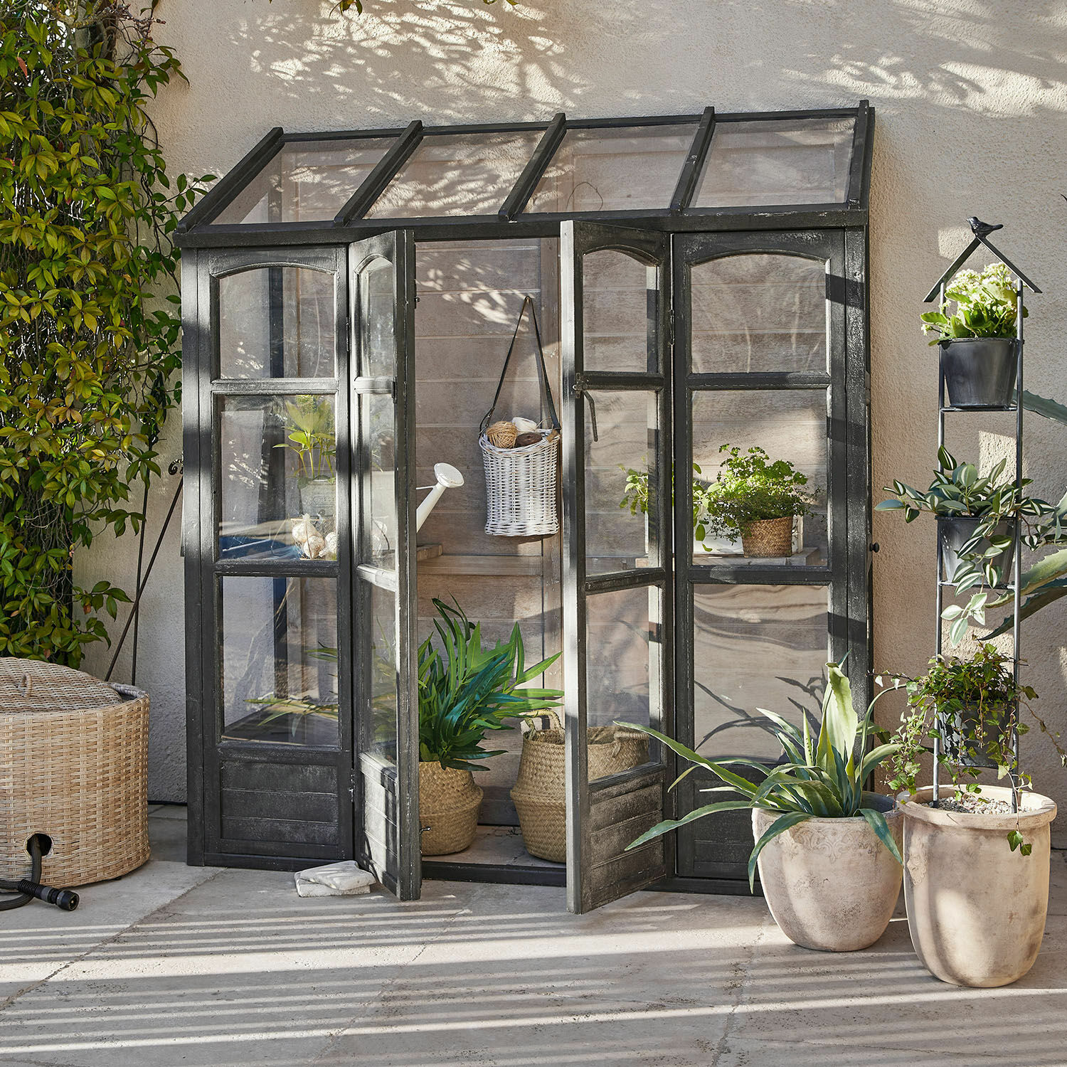 Gewächshaus Abilenne Kleine Gartengewächshaus mit schwarzem Metallrahmen und Pflanzen in Töpfen auf der Terrasse