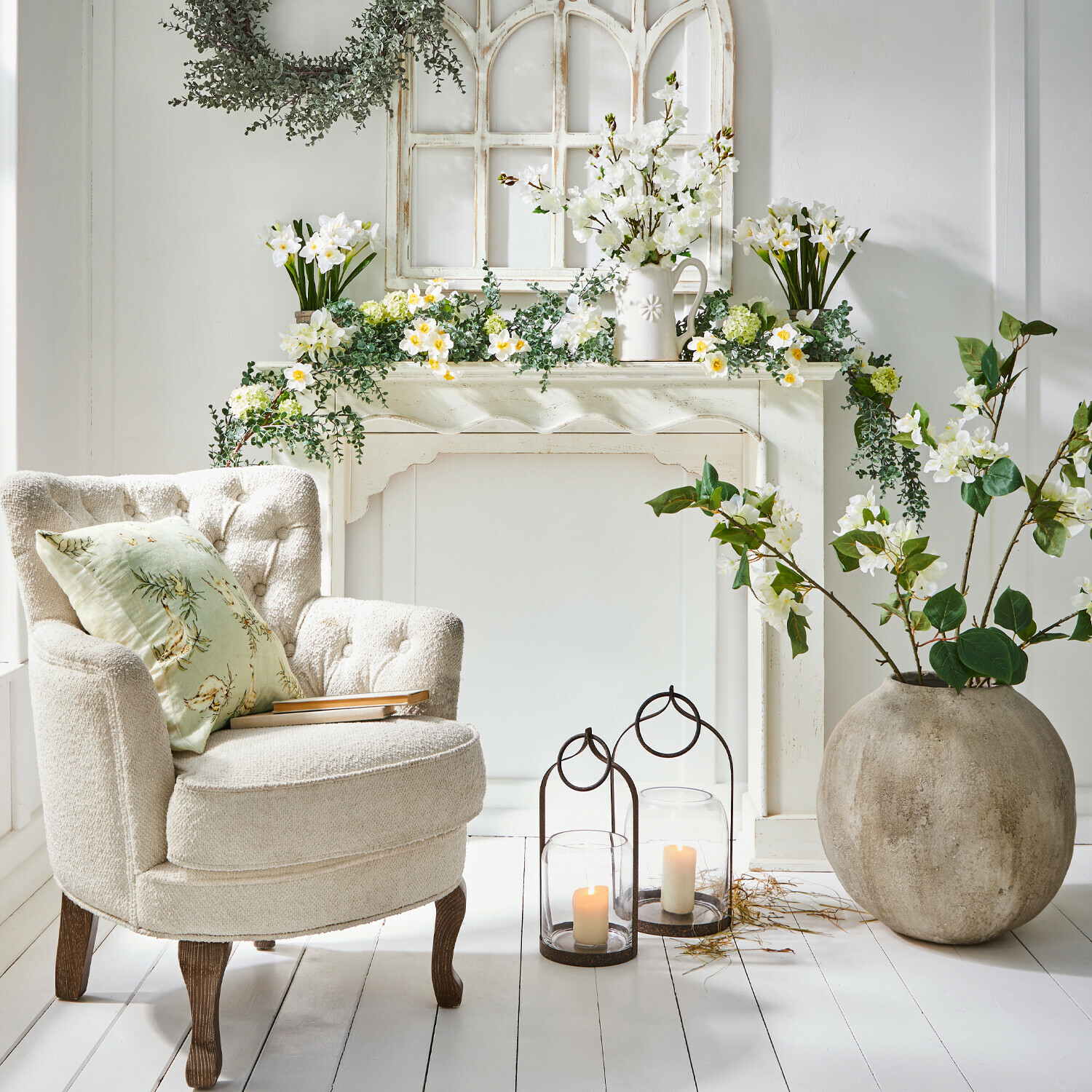 Bequemer cremefarbener Sessel mit Holzbeinen neben dekorativem Kamin mit weißen Blumen und Kerzen