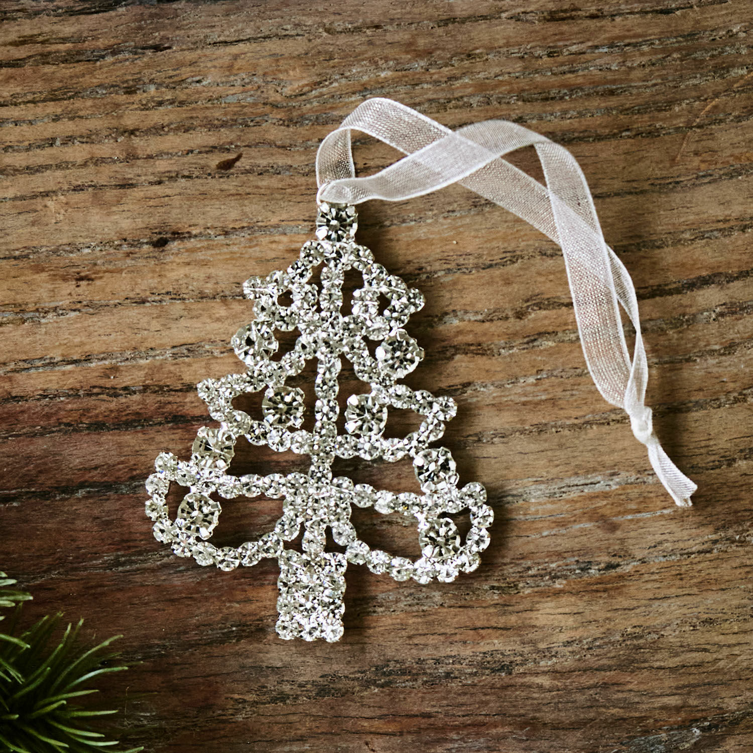 Funkelnder Christbaumschmuck in Baumform aus Kristallen mit weißem Band auf Holzhintergrund