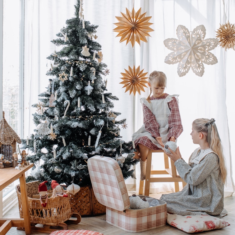 Kinder neben geschmücktem Weihnachtsbaum mit natürlichen Dekorationen und Papiersternen in hellem Raum