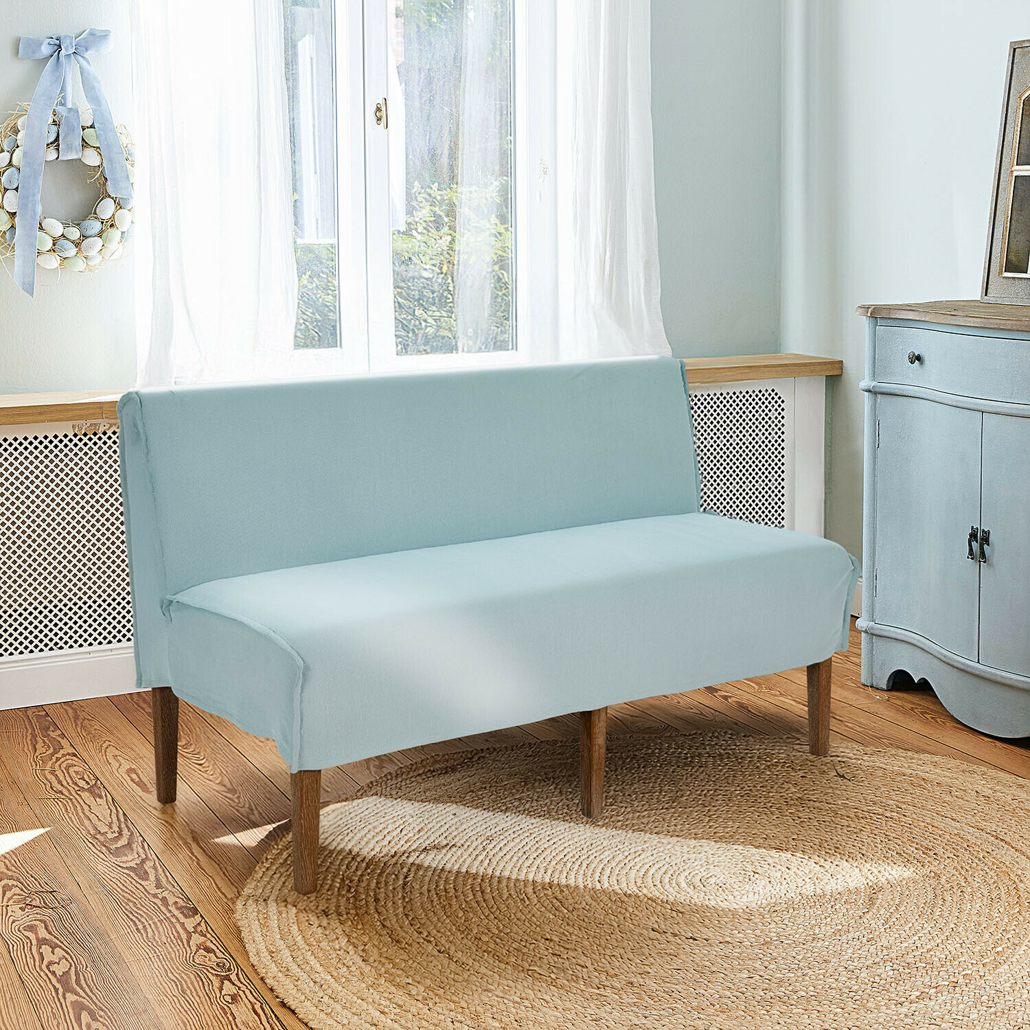Hellblaue Baumwollsofaüberwurf mit Holzbeinen in hellem Wohnzimmer mit Jute-Teppich
