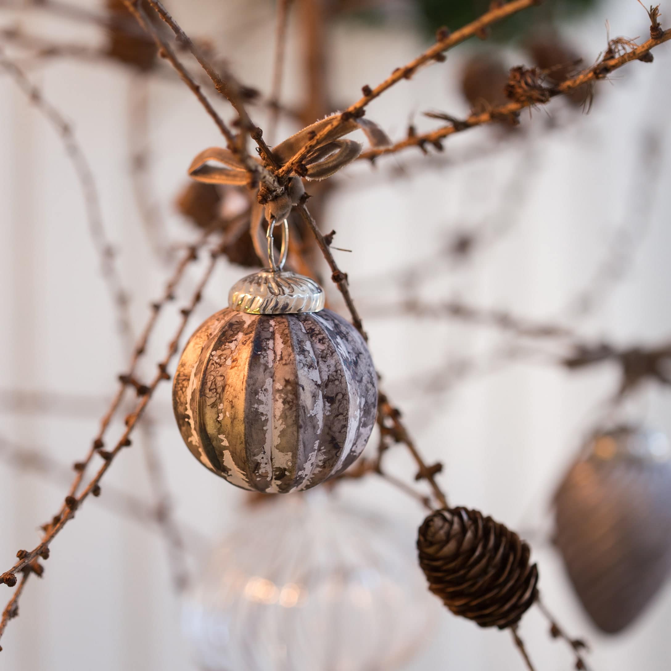 Glas-Weihnachtskugel in Braun-Grau an Zweig mit dekorativer Kieferzapfen-Hängung