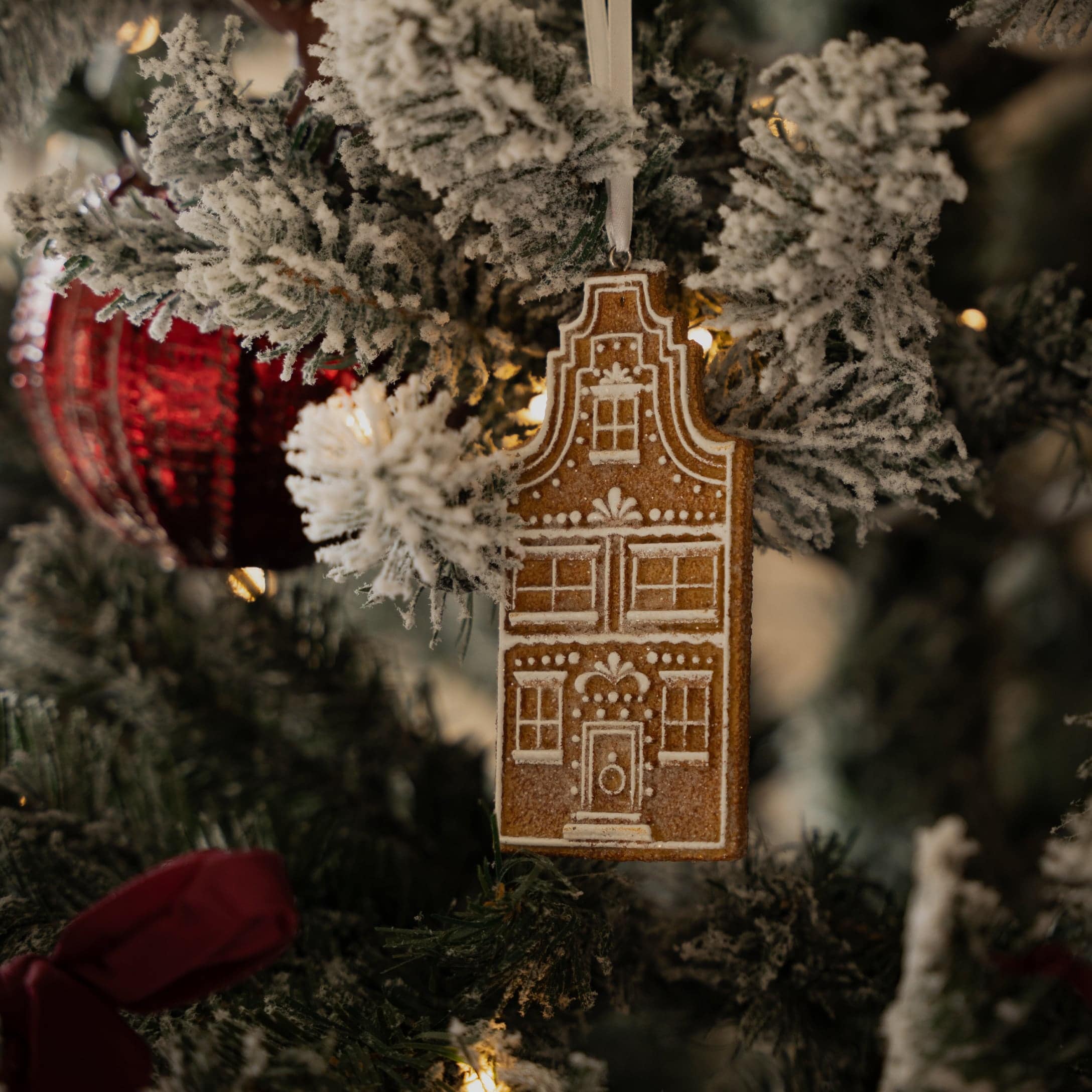 Lebkuchen-Hausanhänger an schneebedecktem Tannenzweig mit rotem Weihnachtsbaumschmuck