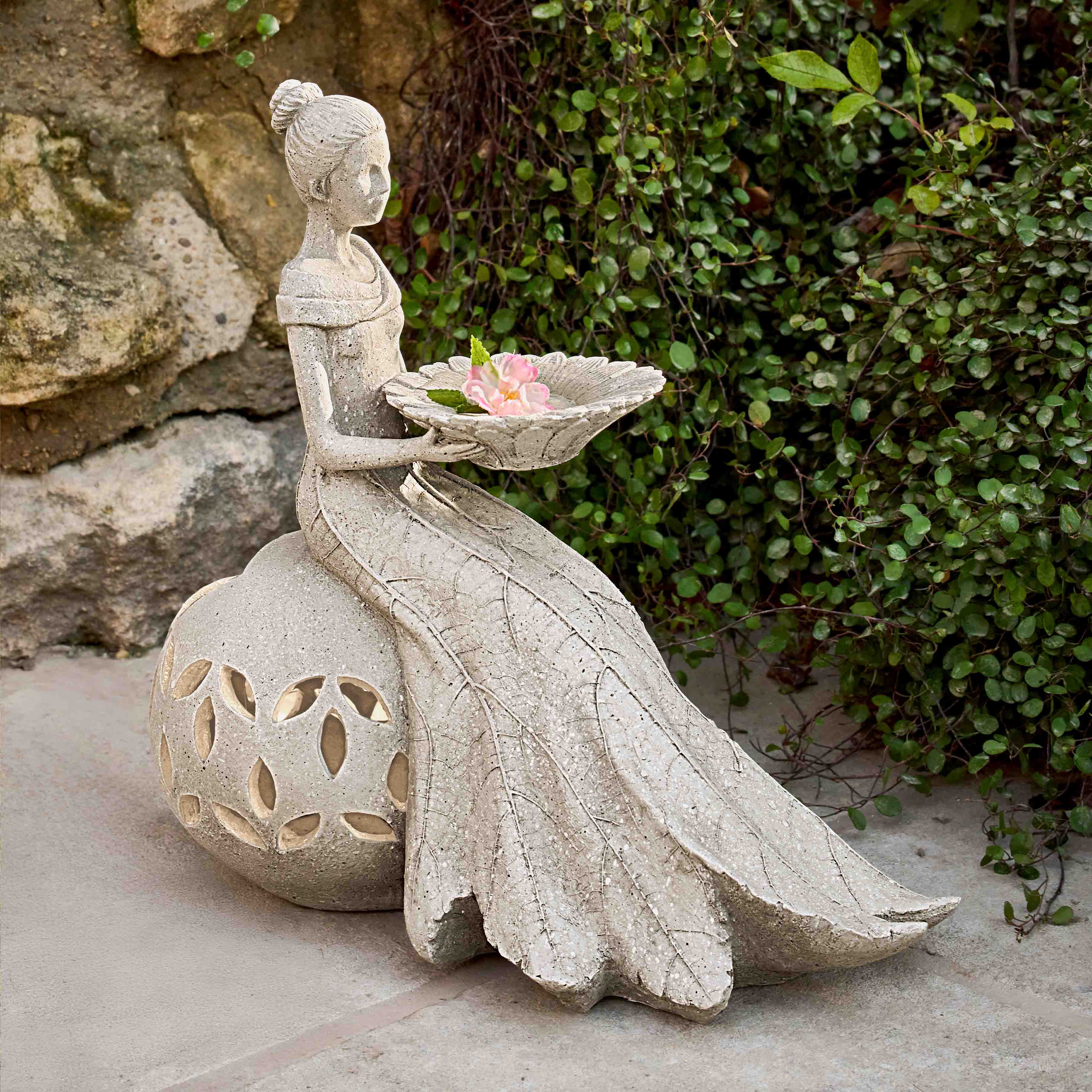 Gartenfigur aus Stein einer sitzenden Frau mit Schale und Blume als dekorativer Gartenschmuck