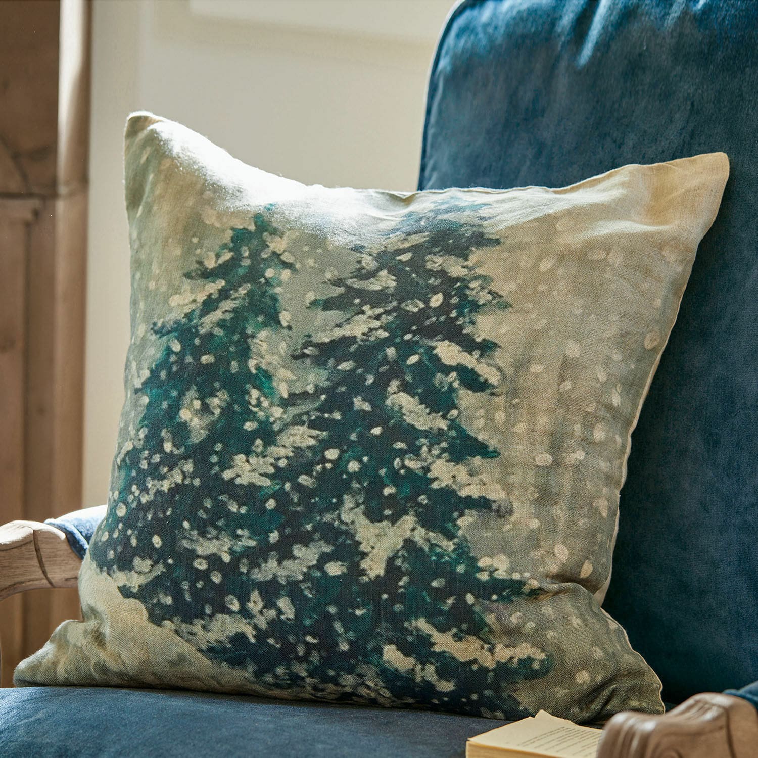 Kissenhülle Mierta Dekoratives Leinenkissen mit Tannenbaum-Motiv in Grün- und Beigetönen auf blauem Sessel