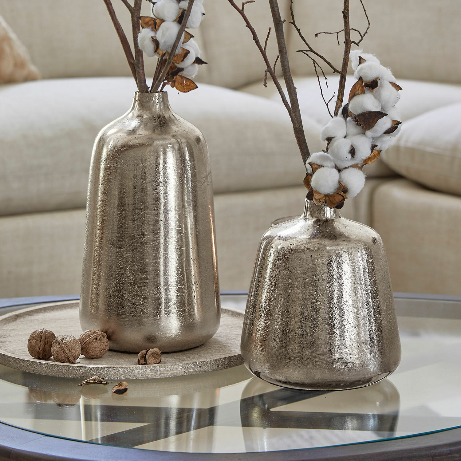 Zwei silberne Metallvasen auf Glastisch mit dekorativen Baumwollzweigen und Walnüssen