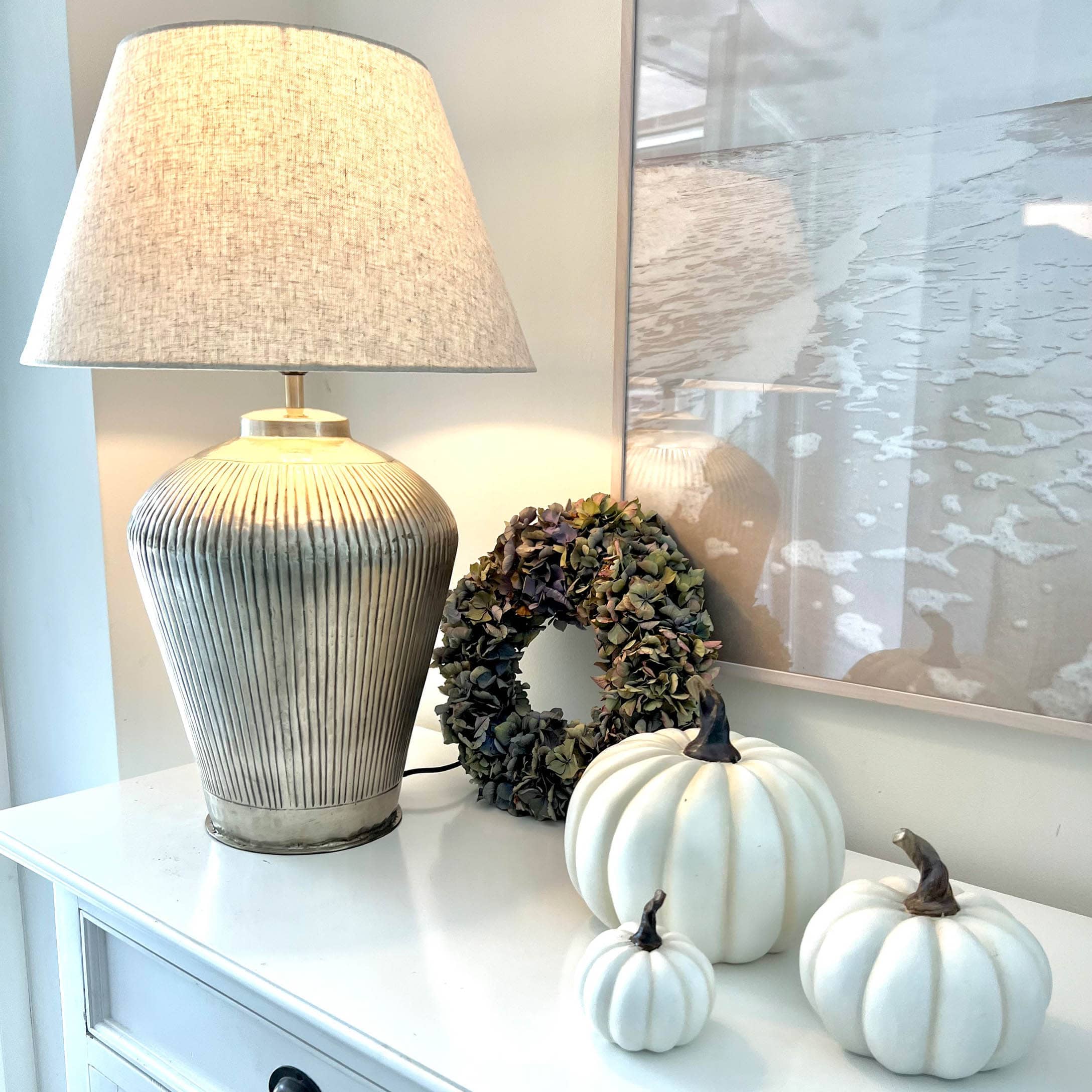 Tischlampe mit beigem Stoffschirm und Keramikfuß, weiße Dekokürbisse und getrockneter Blumenkranz