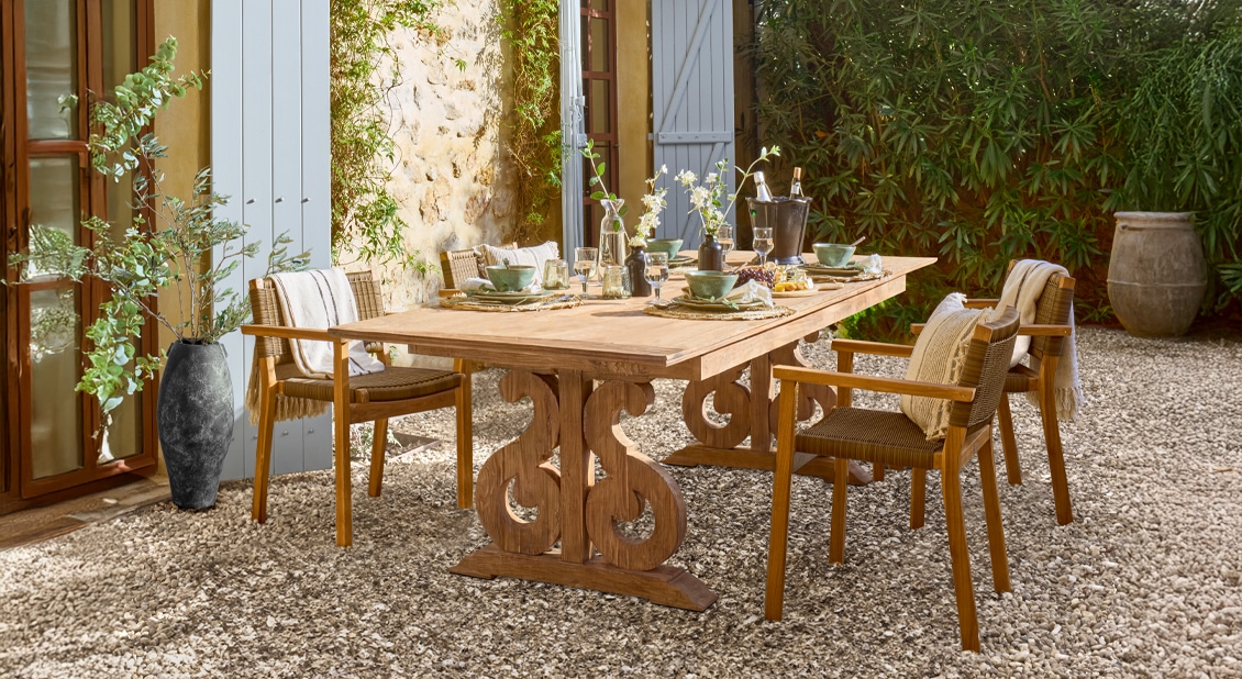 Holz-Gartentisch mit geschnitztem Fuß und Stühlen auf Kiespatio im mediterranen Stil