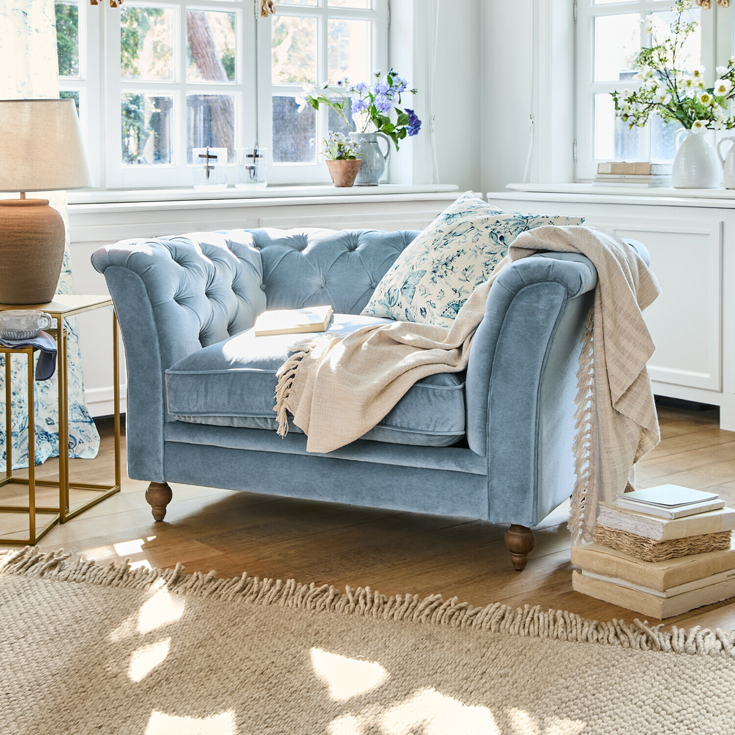 Zweisitziges Sofa aus blauem Samt mit gesteppter Rückenlehne und beiger Decke in hellem Wohnzimmer