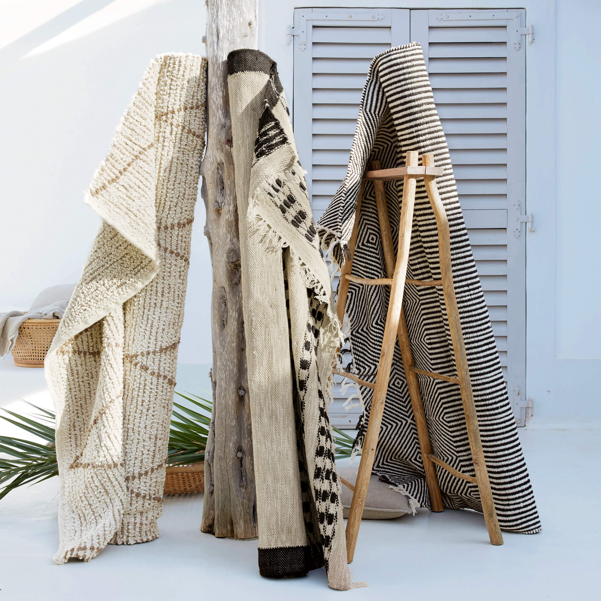 Drei dekorative Teppiche aus Naturmaterialien in Beige-Schwarz-Mustern auf heller Terrasse