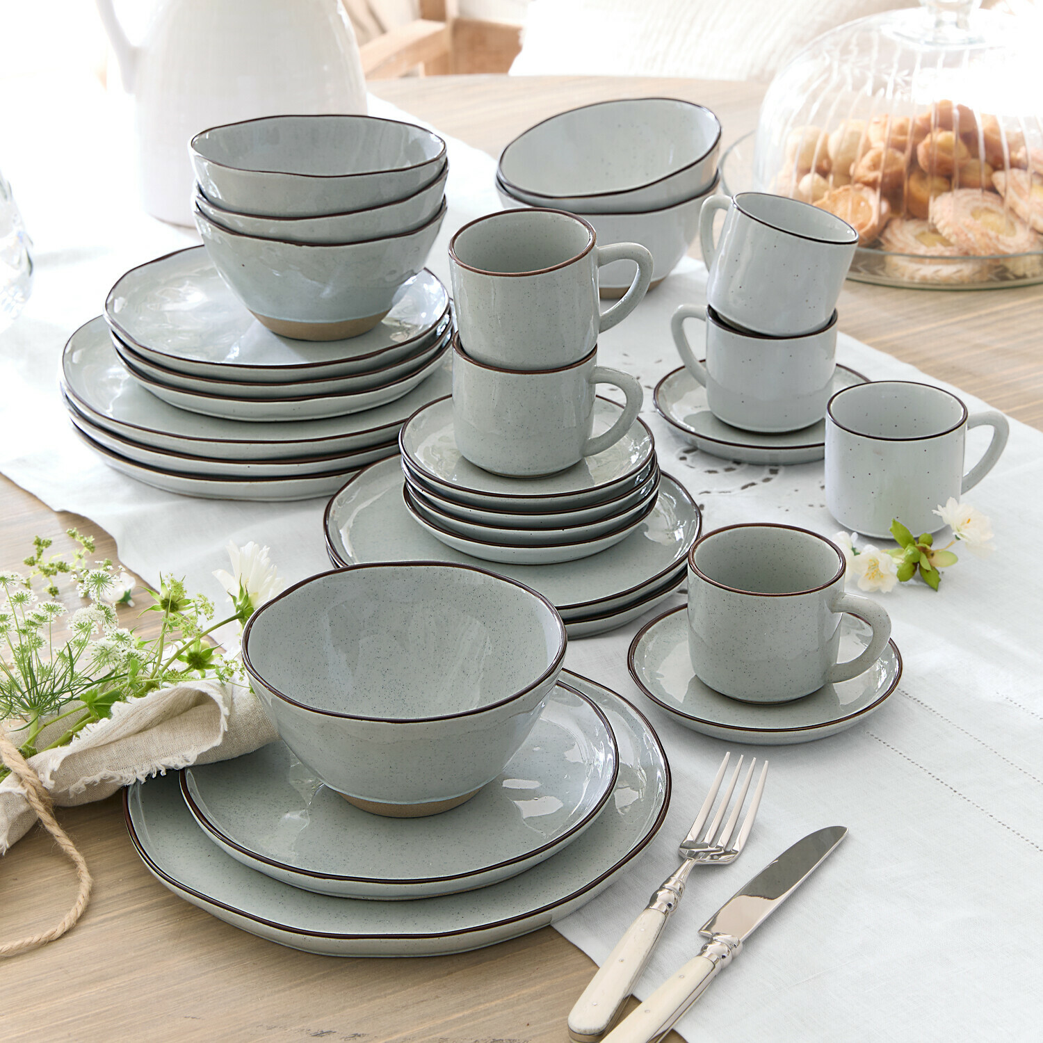 Graues Keramik-Geschirrset mit braunem Rand, Teller, Schalen und Tassen auf dem Tisch arrangiert