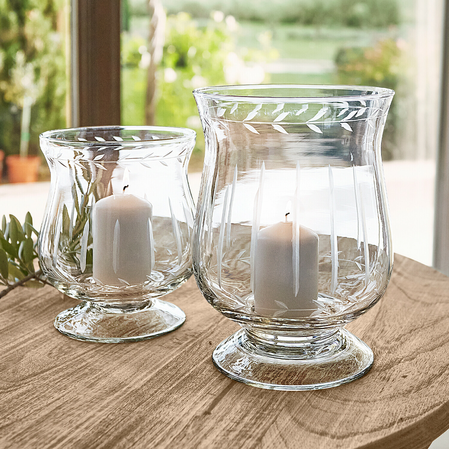 Windlicht 2er Set Moon Zwei transparente Glaswindlichter mit weißen Kerzen auf Holztisch, dekoratives Blattmuster