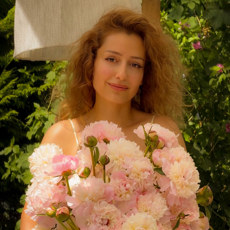Frau mit langen Haaren hält großen Strauß rosa Pfingstrosen vor grünem Gartenhintergrund