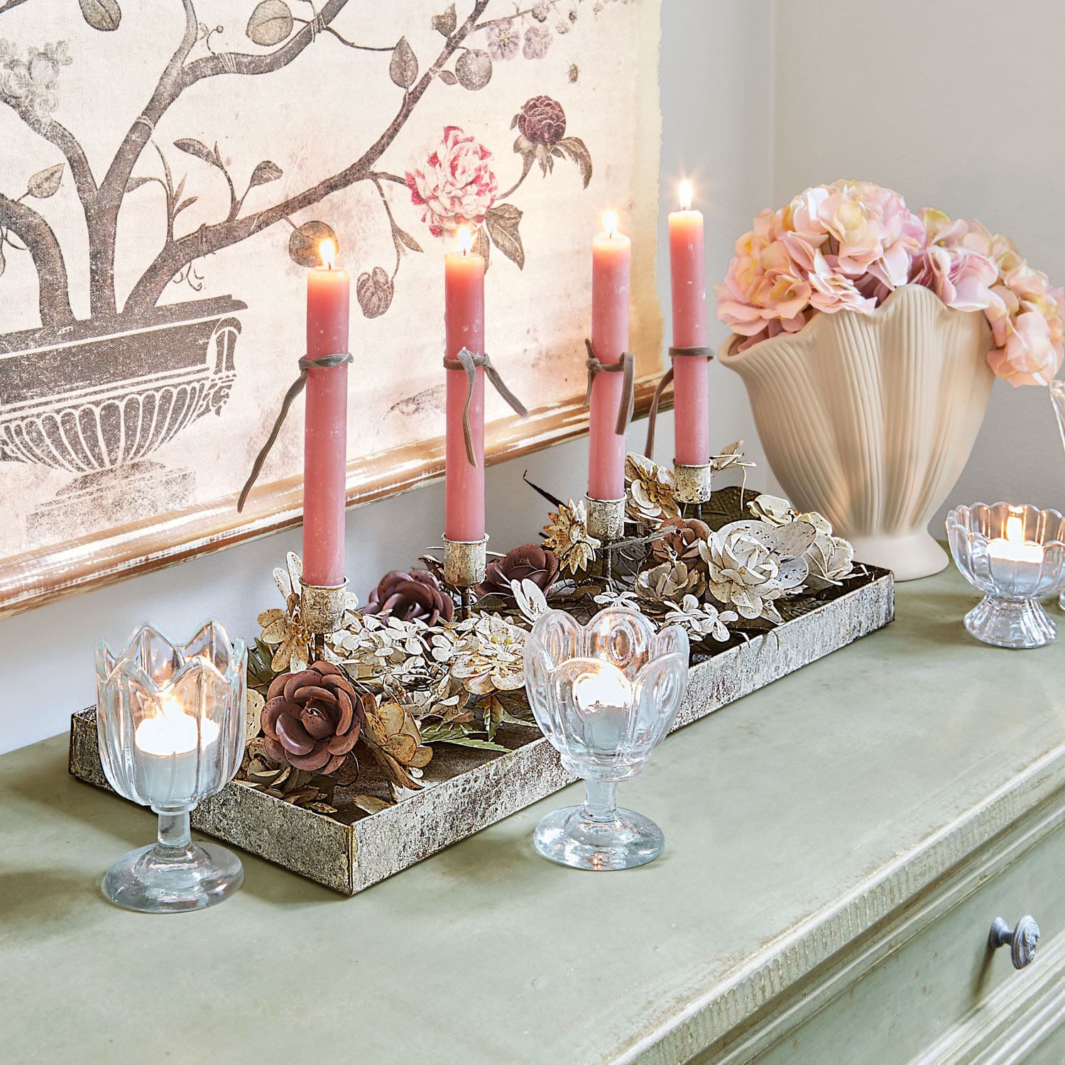 Dekorativer Kerzenhalter mit Metallblumen und rosa Kerzen auf grünem Tisch mit Vase