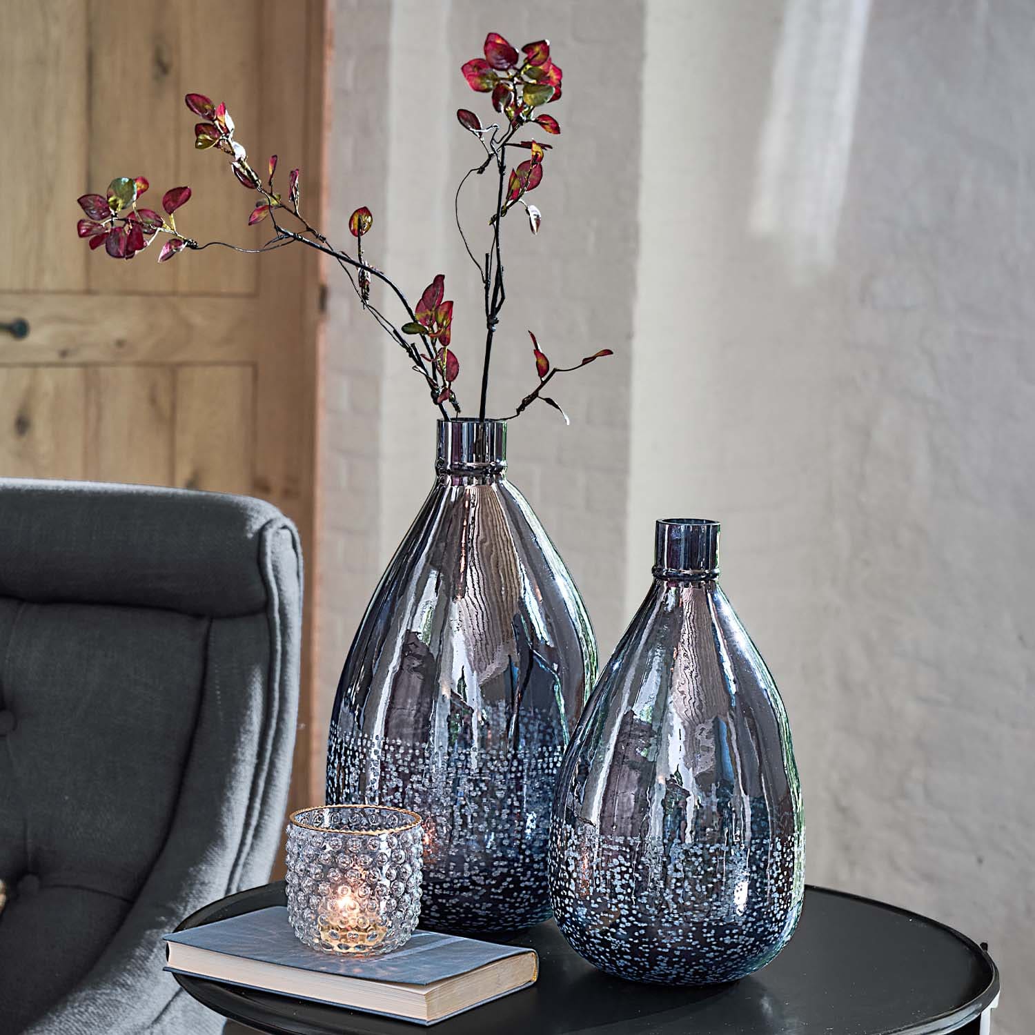 Zwei dekorative Rauchglasvasen mit Blasenmuster auf schwarzem Tisch neben Kerzenhalter und Buch