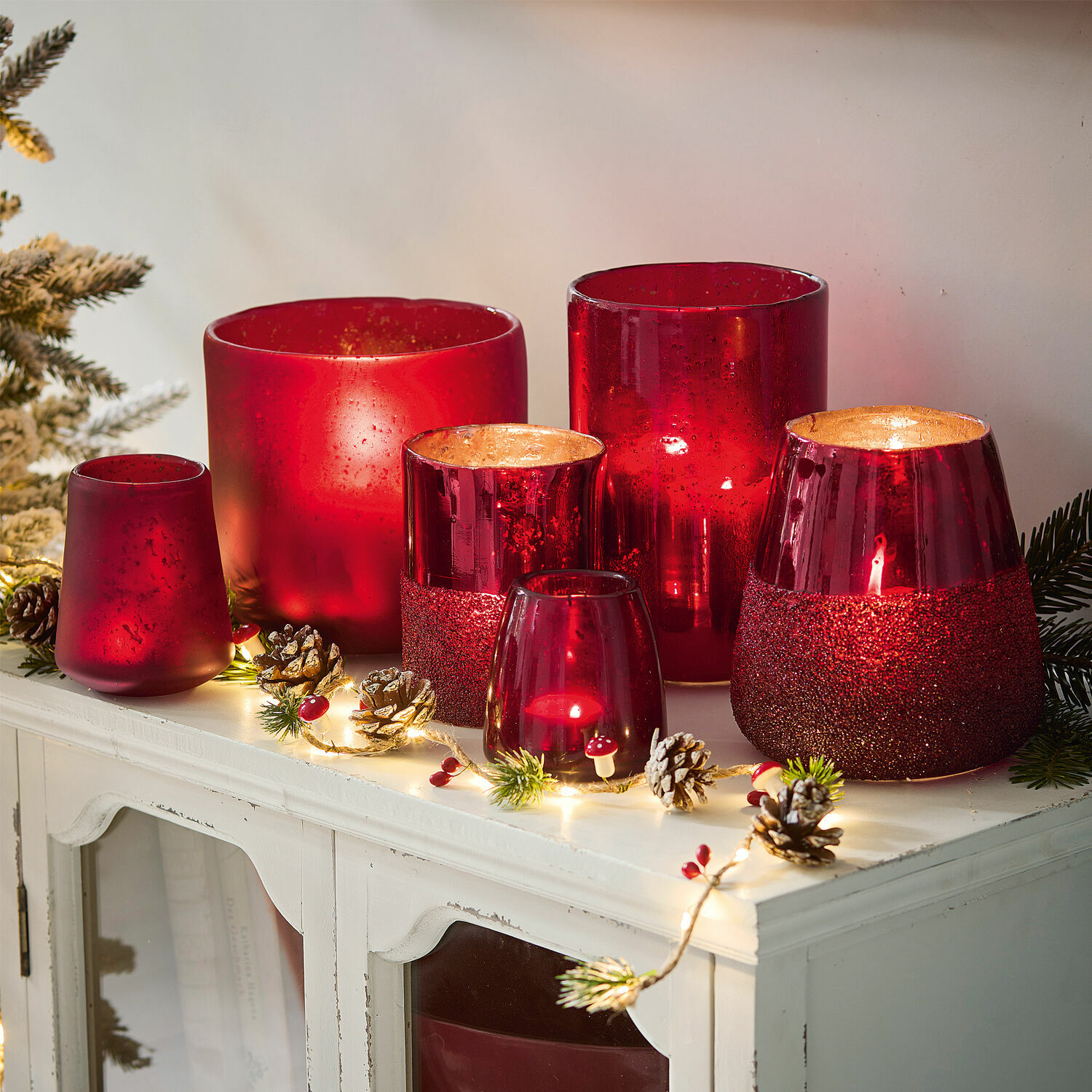 Windlicht 6er Set Paro Set aus roten Glaswindlichtern in verschiedenen Formen auf weißem Schrank mit Weihnachtsdeko