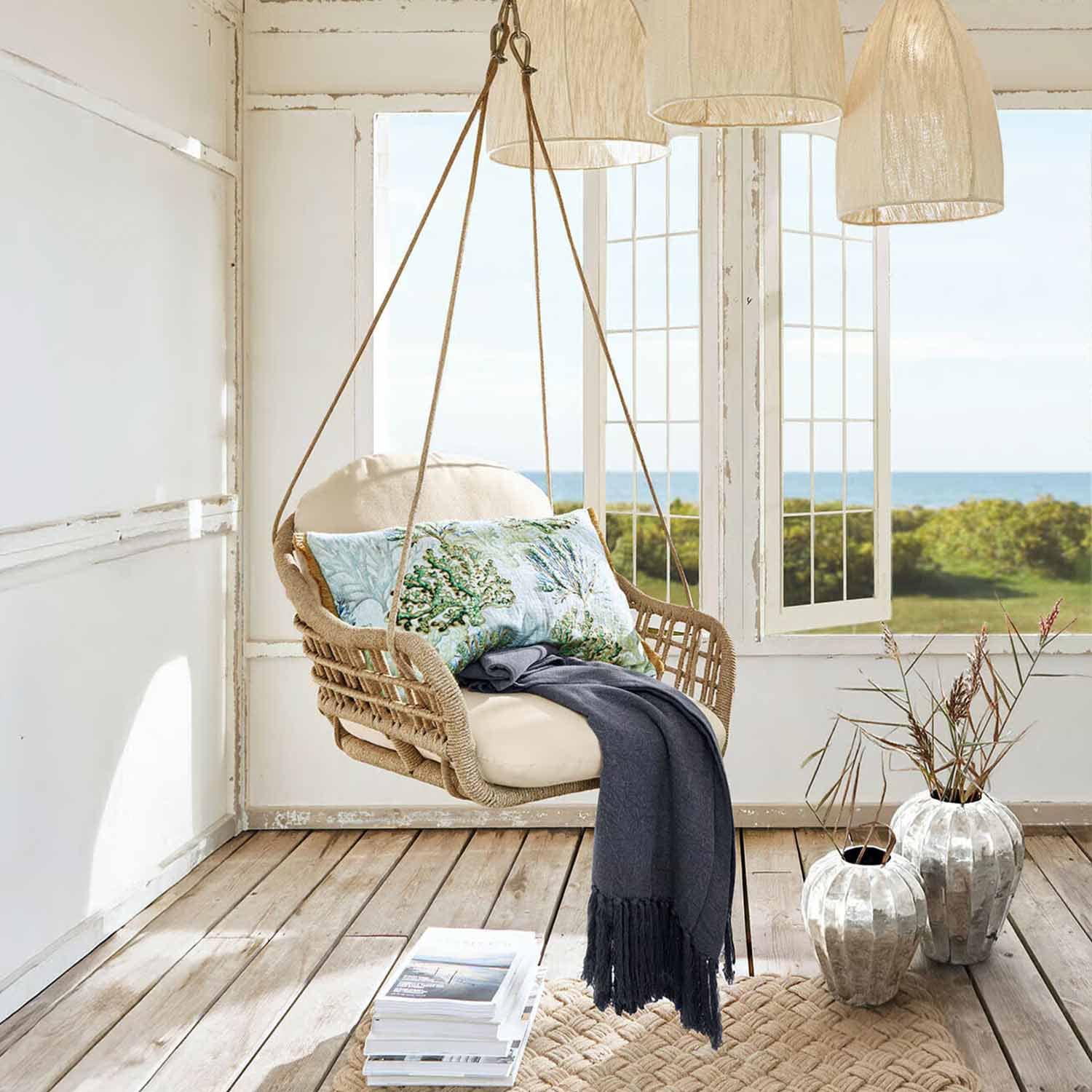 Hängesessel aus geflochtenem Seil in Naturfarbe mit cremefarbenem Kissen und dunkelblauer Decke in hellem Raum