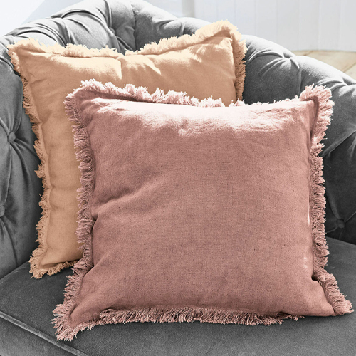 Zwei dekorative Leinenkissen in Rosa und Beige mit Fransen auf grauem Sofa, gemütliches Ambiente