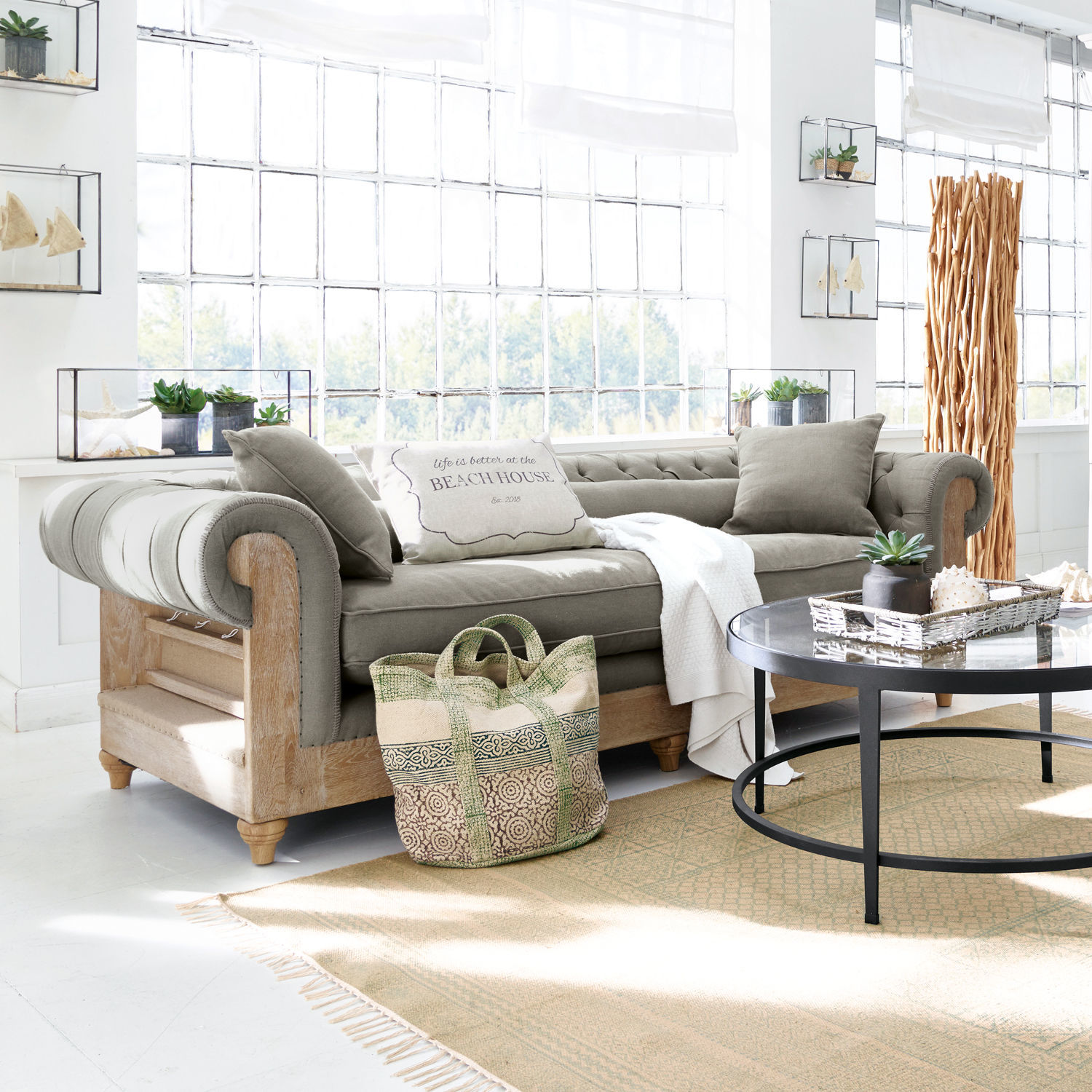 Sofa Kanani Graues Sofa mit Holzrahmen in hellem Wohnzimmer mit Dekorationen und großem Fenster