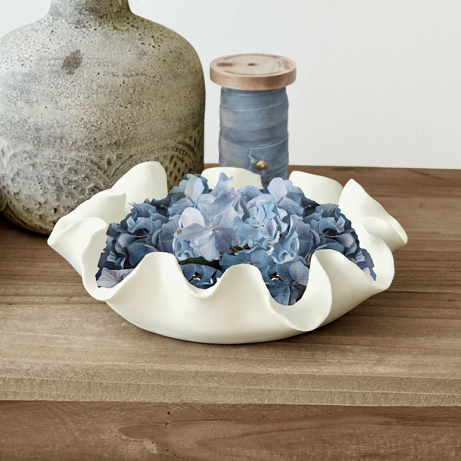 Weiße Keramikschale mit welligem Rand und blauen Blumen auf Holztisch