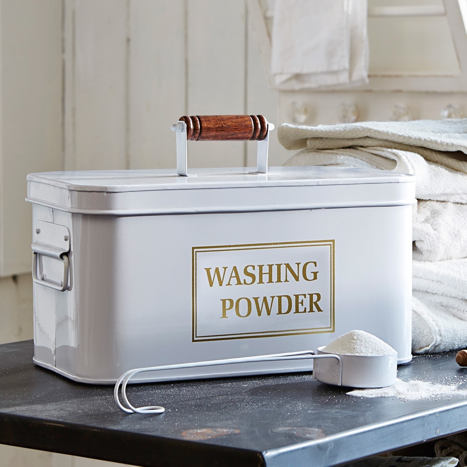 Waschmittelbehälter Washing Weißer Metallbehälter für Waschpulver mit Holzgriff und Messlöffel auf schwarzem Tisch