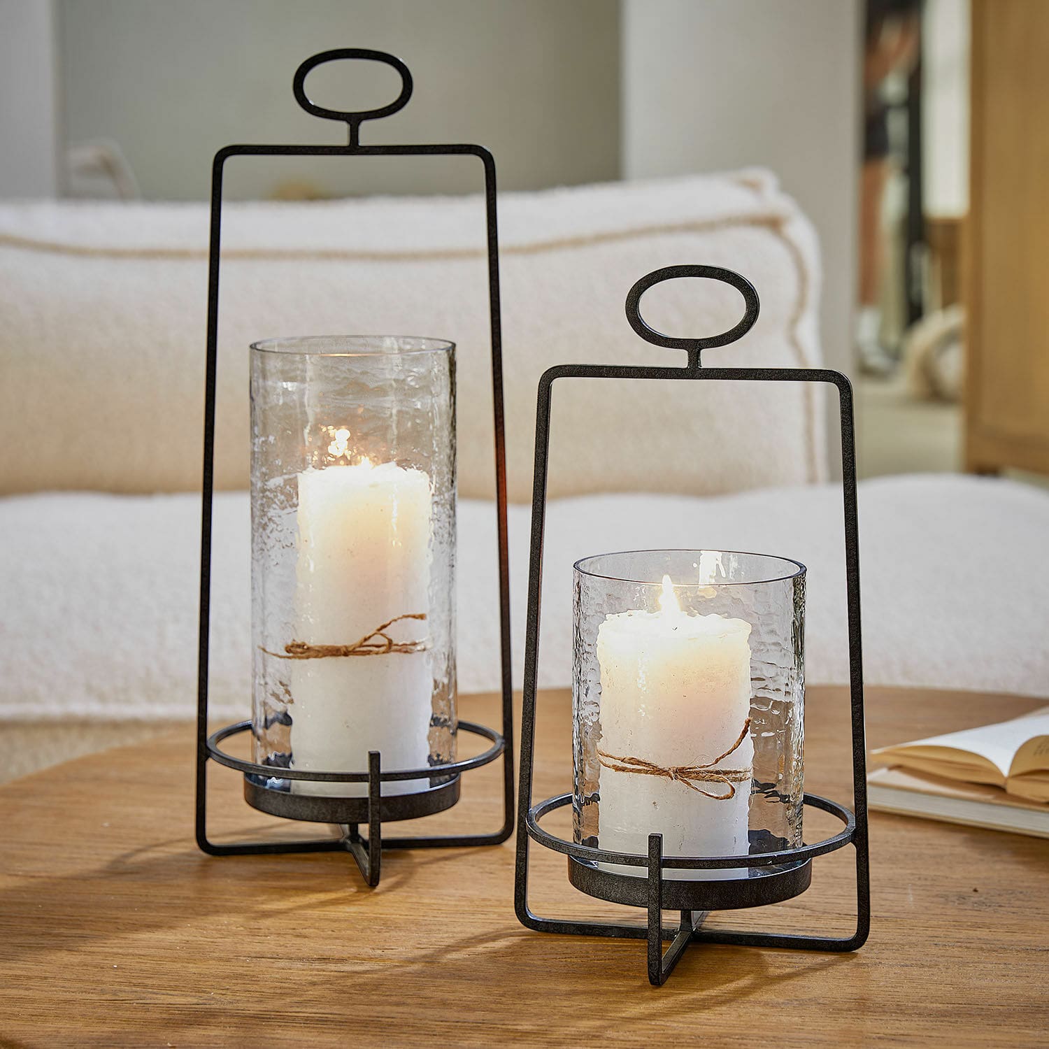 Windlicht 2er Set Zevara Zwei Metalllaternen mit klarem Glas und weißen Kerzen auf Holztisch im Wohnzimmer