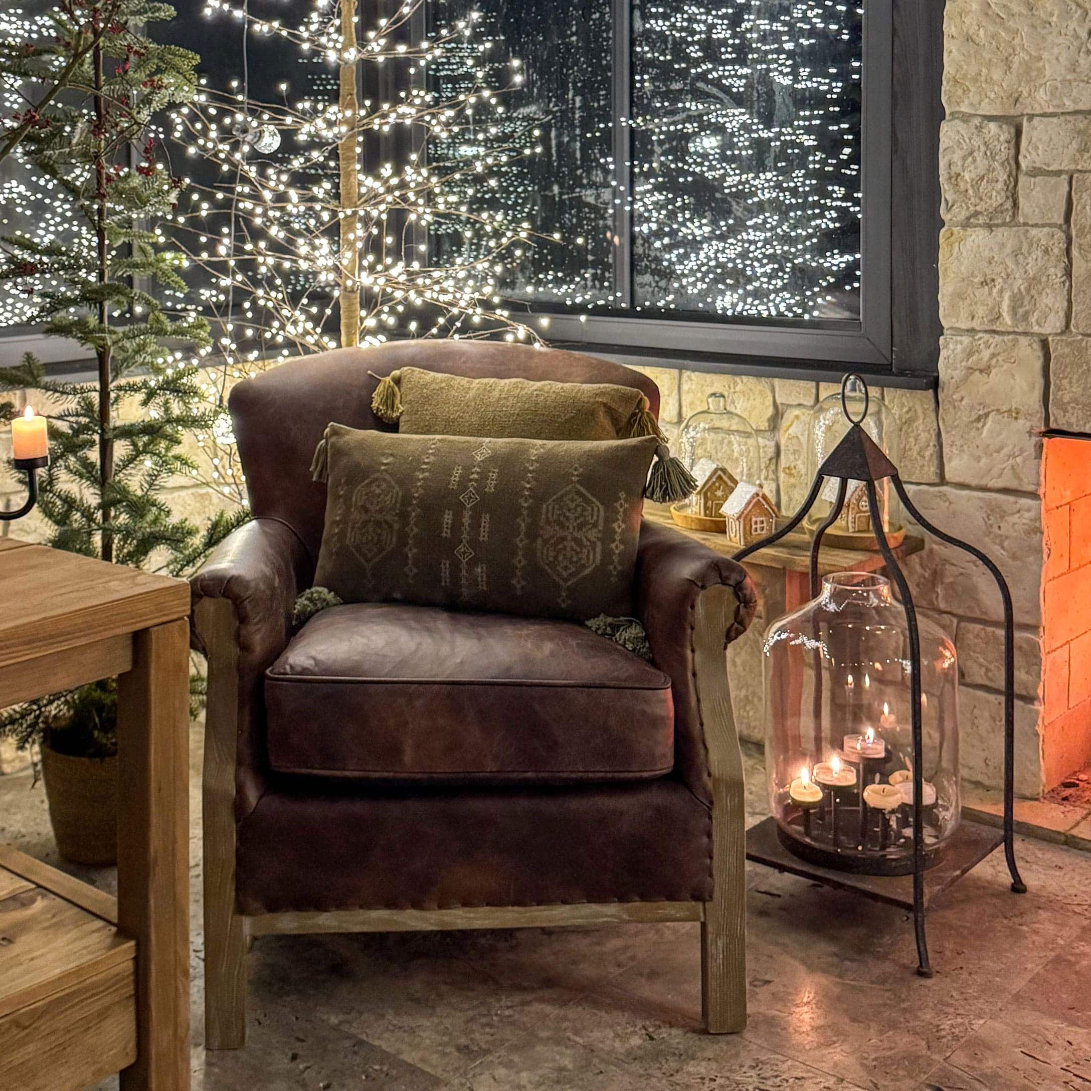 Brauner Ledersessel mit grünen Kissen in weihnachtlicher Atmosphäre mit Lichterketten und Kerzen