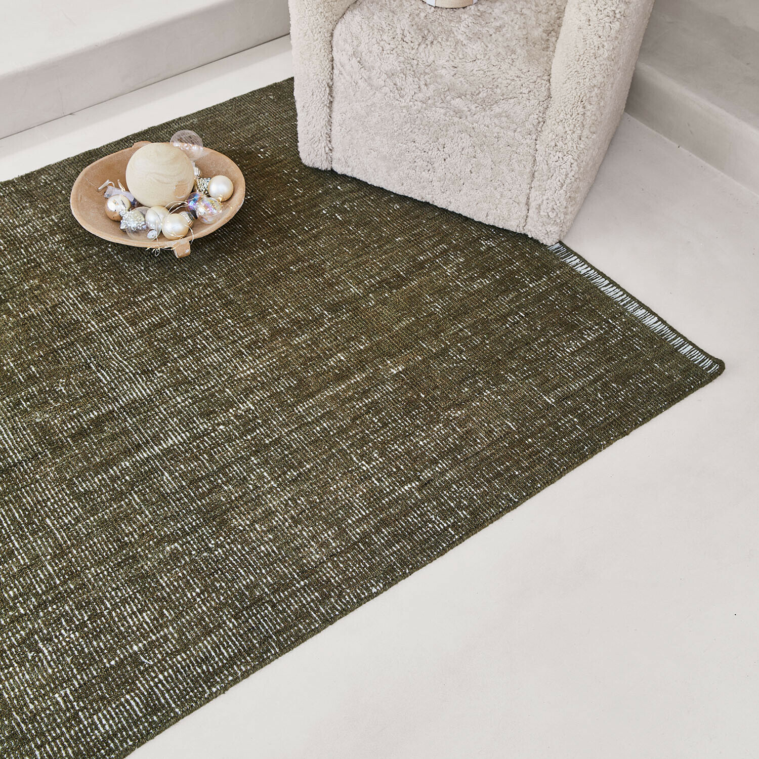 Grüner Teppich mit feinem Muster neben cremefarbenem Sessel und Dekoration auf dem Boden