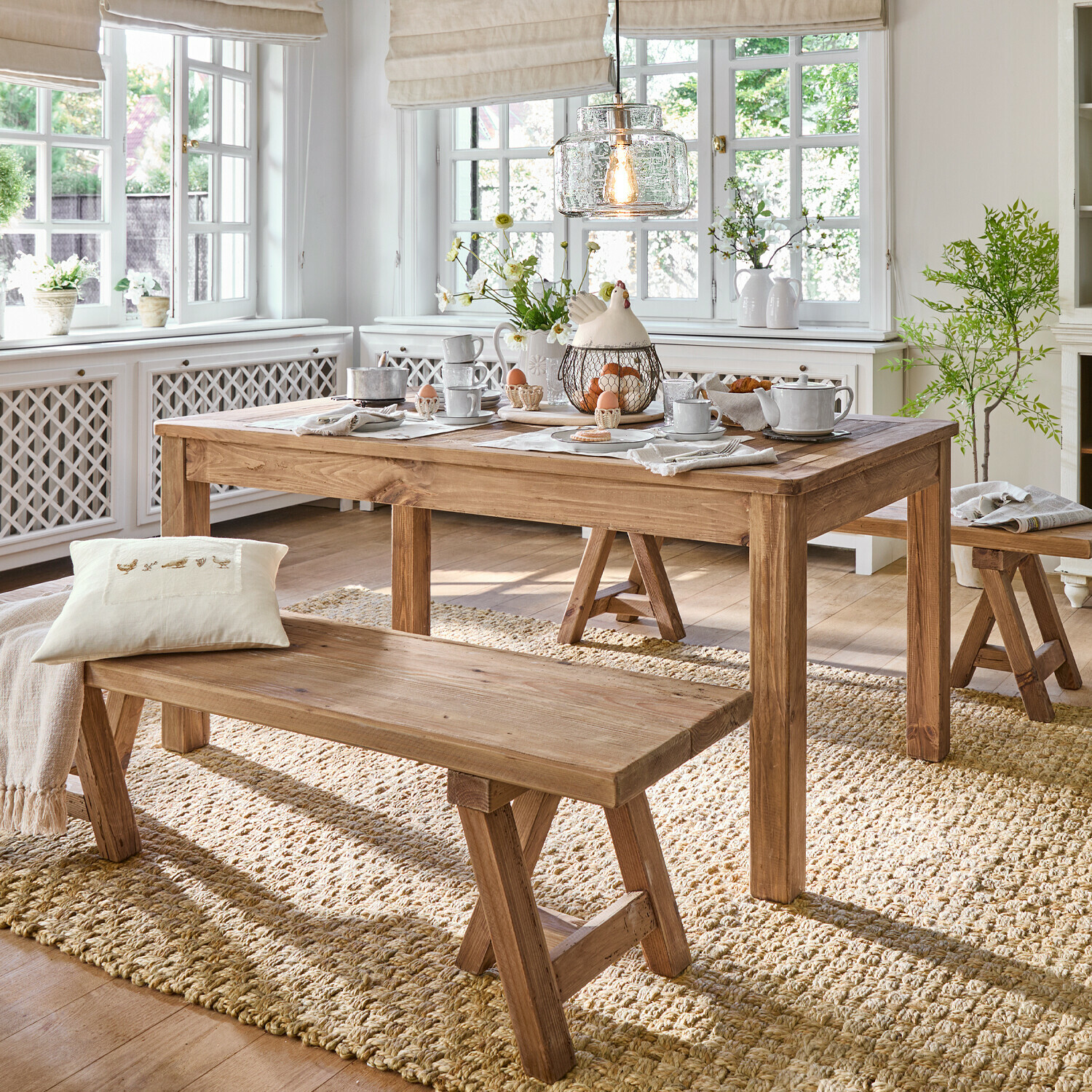 Esszimmer mit Holztisch und Bänken auf Naturteppich, helles Interieur mit Dekorationen und Licht